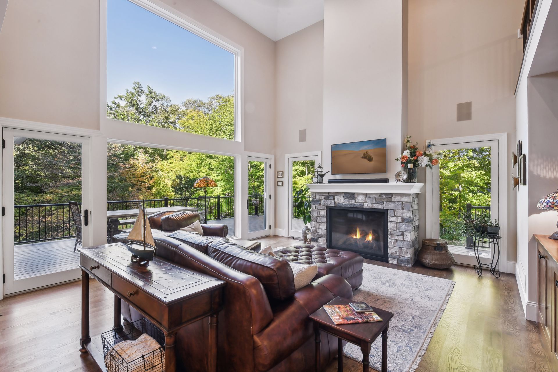 Living room with tall windows, fireplace, leather couch, and view of trees.