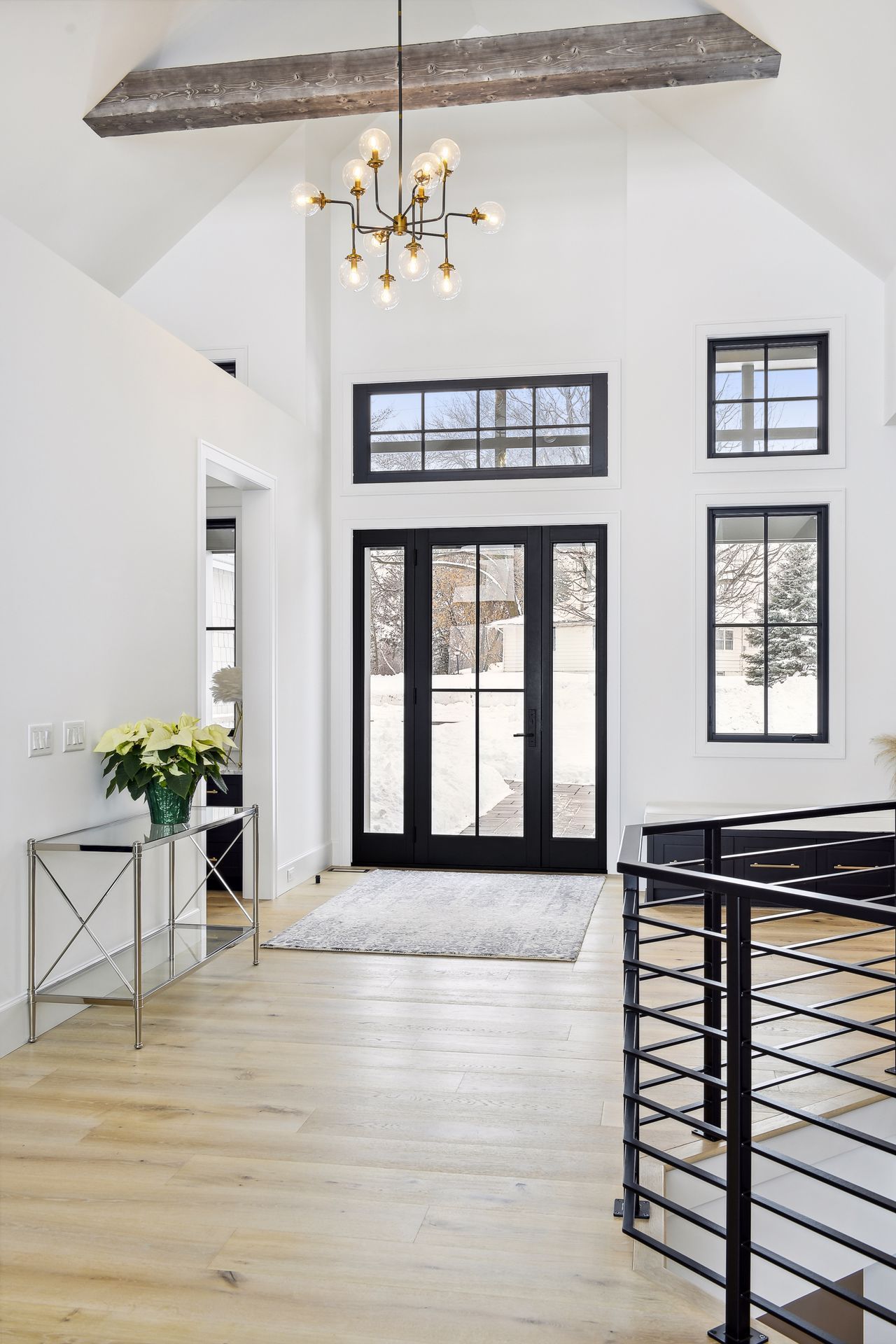 Bright entry hall with black-framed windows and doors, light wood floors, and a modern chandelier.