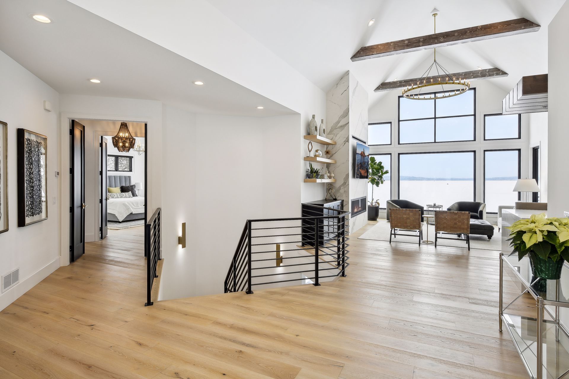 Spacious hallway with light wood floors, leading to a living room with large windows overlooking a body of water.