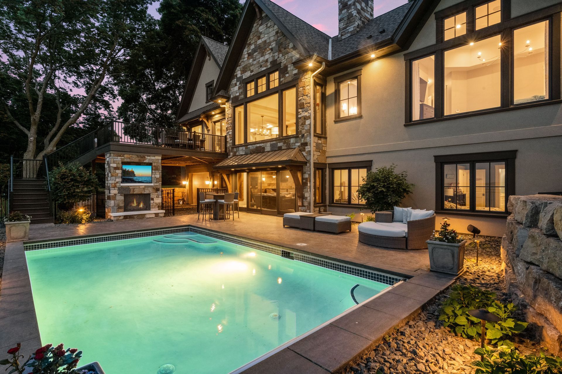 Luxury home exterior with pool and outdoor entertainment area at dusk.