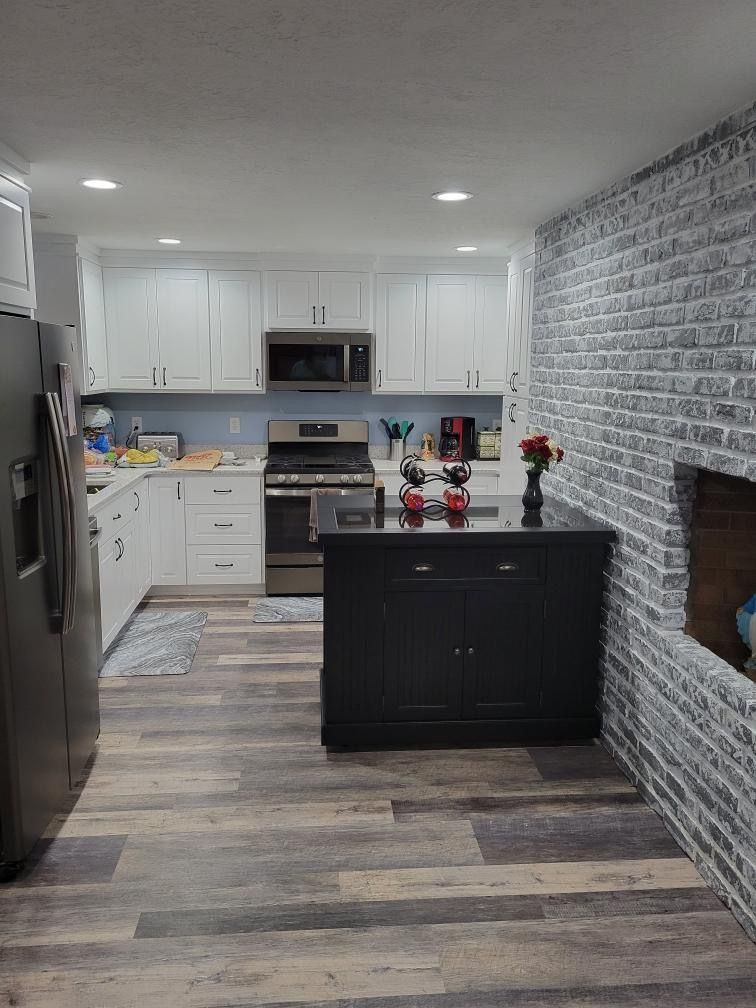 Kitchen with white cabinets, black island, stainless steel appliances, and faux painted brick wall.