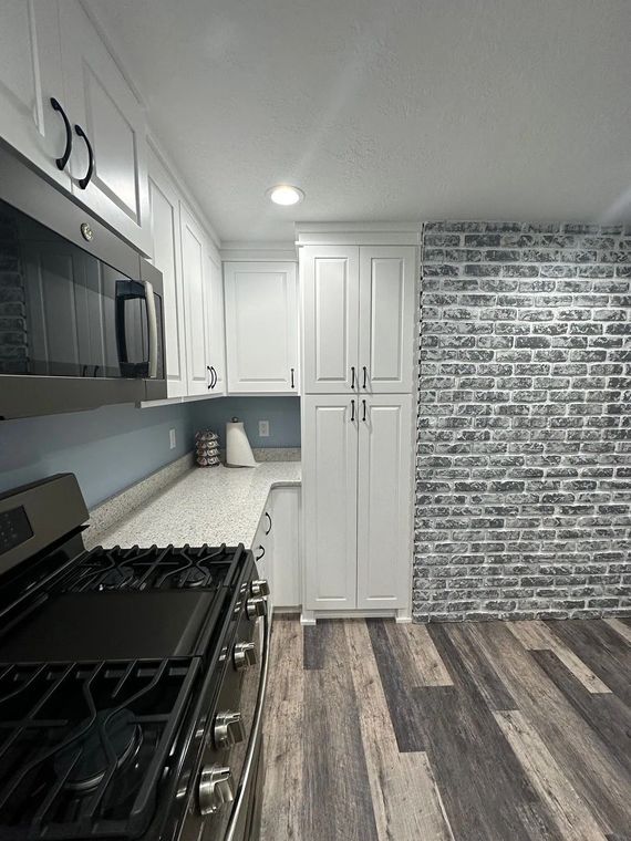 White kitchen with gas stove, granite countertops, and brick accent wall.