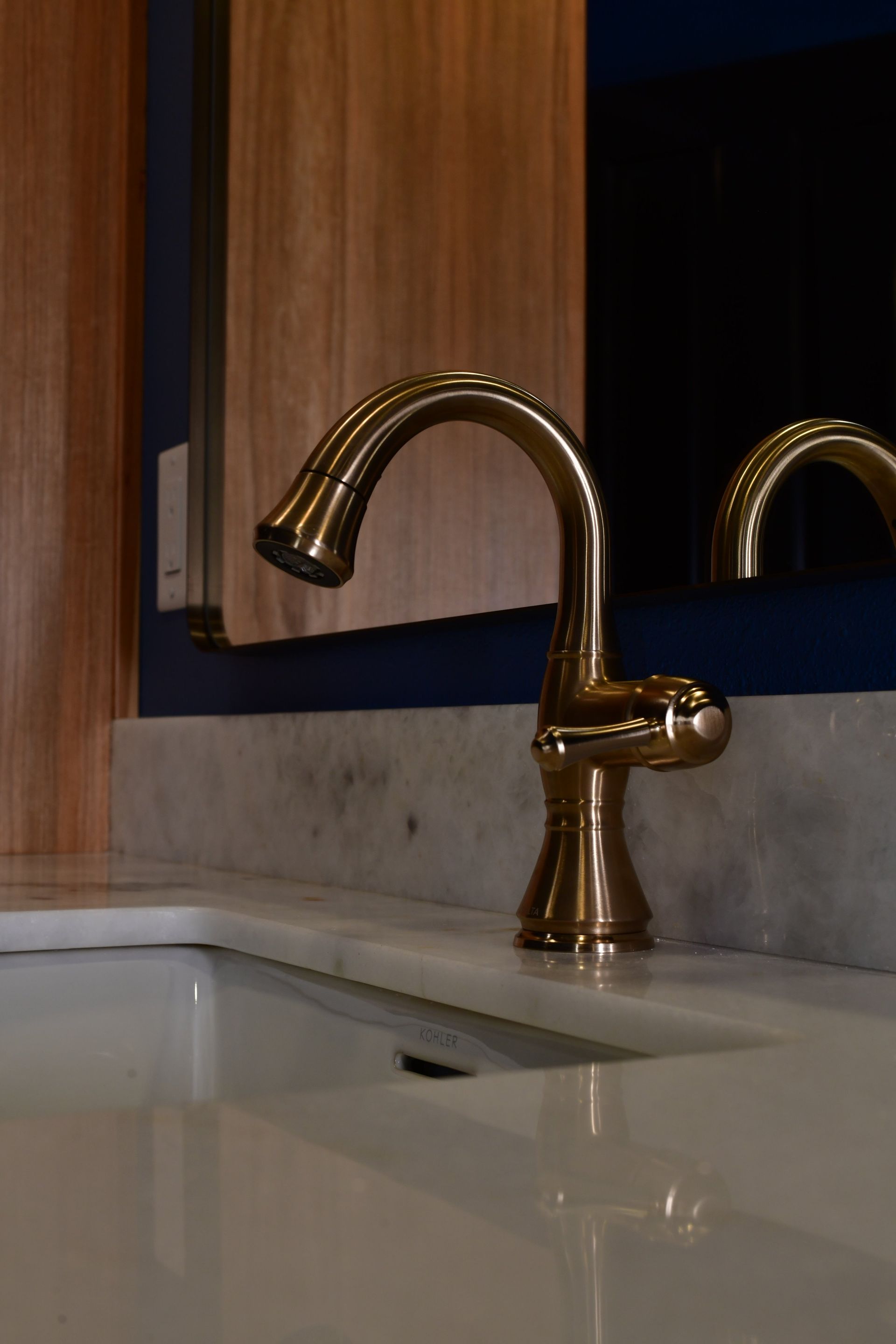 Gold faucet over a white sink, set against wood cabinets and a dark blue background.