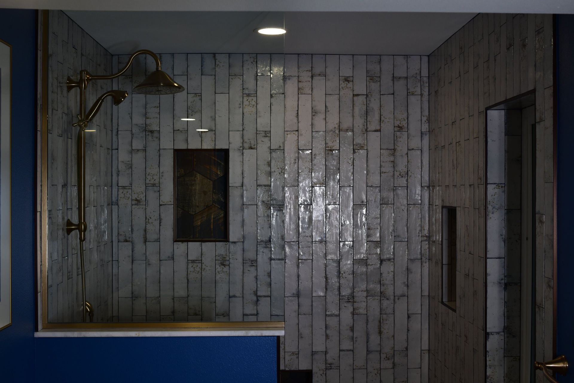 Shower with wood-look tile walls, gold showerhead, and inset shelves. Blue wall below.