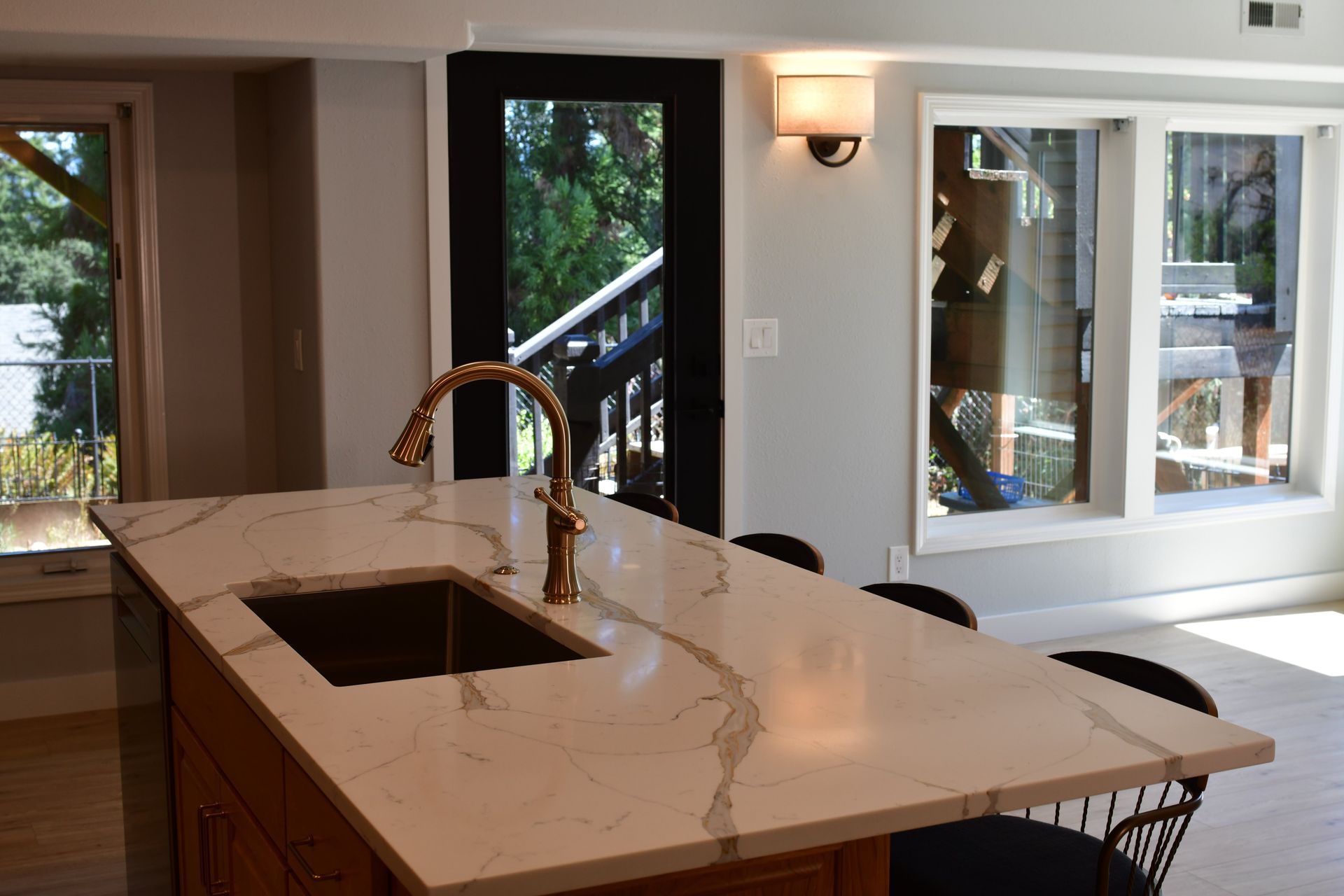 Kitchen island with gold faucet and marble countertop, black door to outside, and windows.