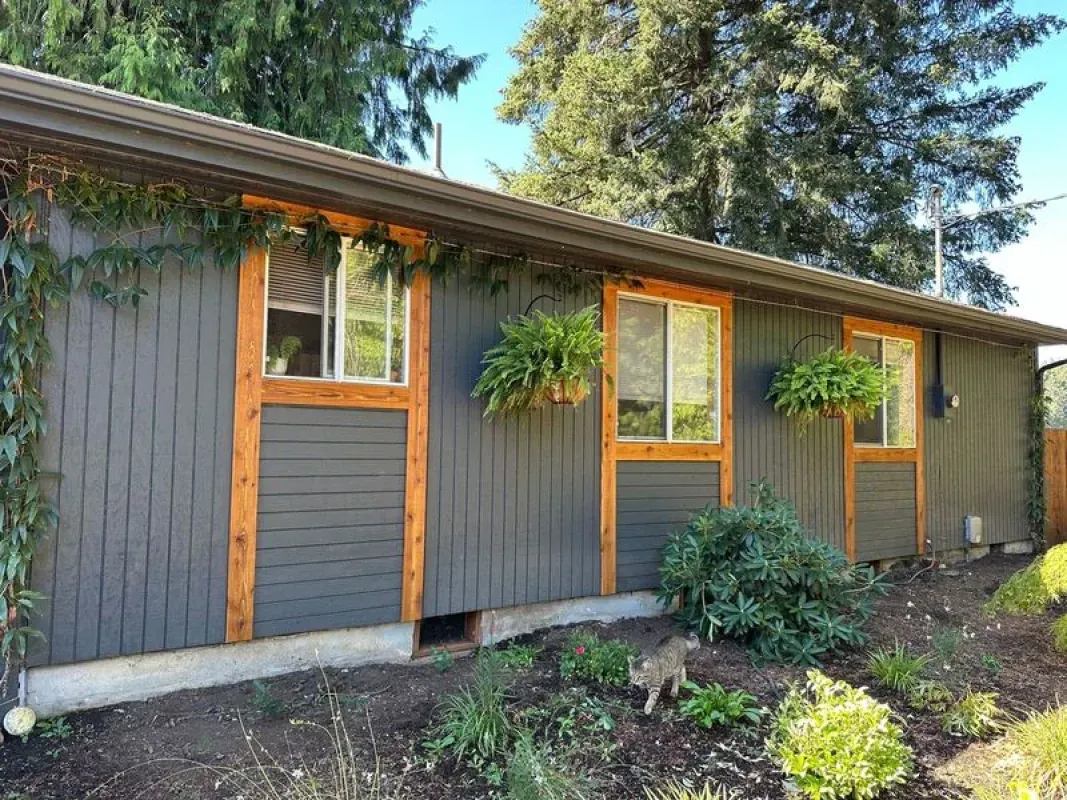 Gray house with wooden window frames and hanging plants.