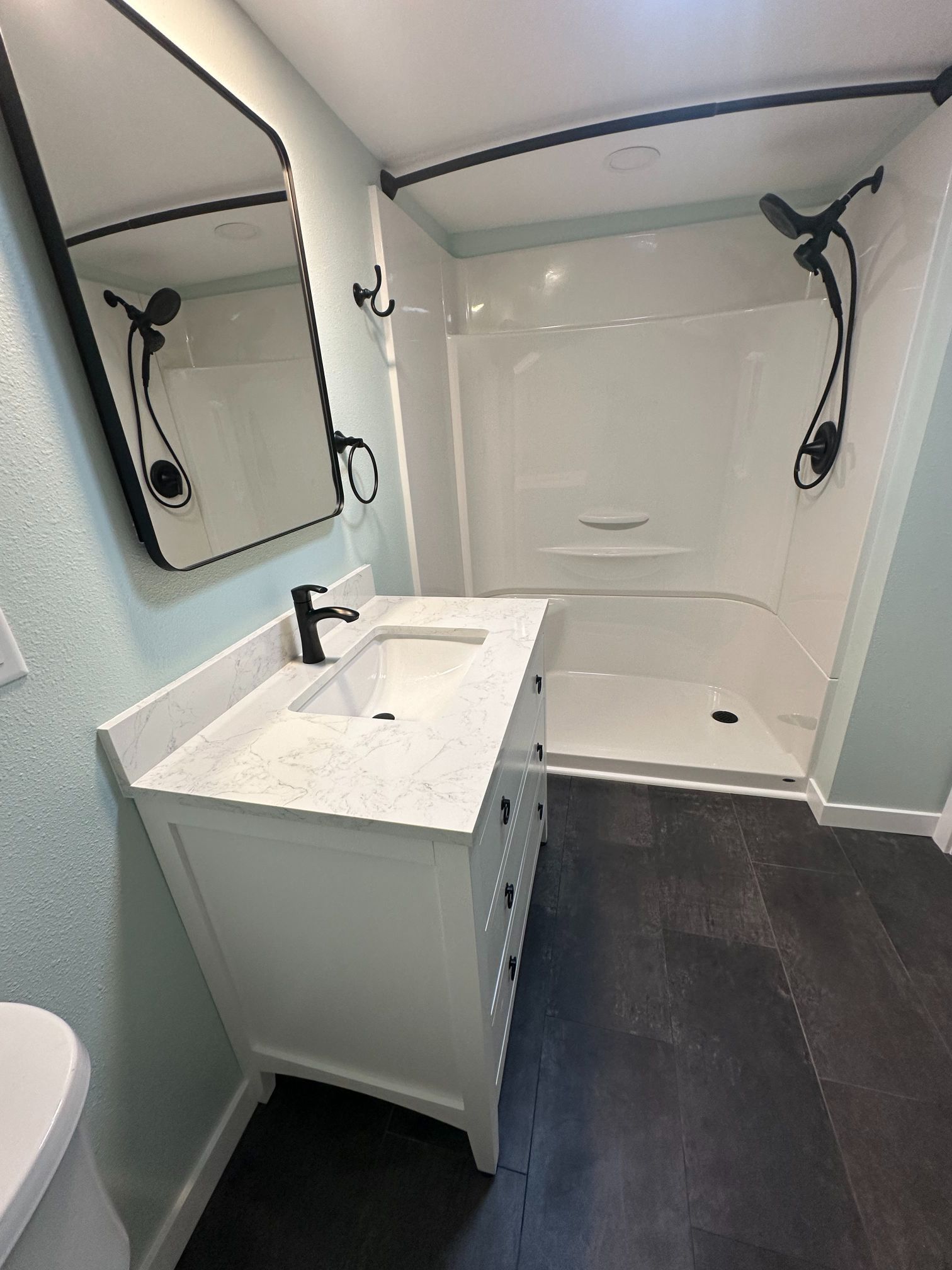 Modern white bathroom with black fixtures, vanity, shower, and dark gray flooring.
