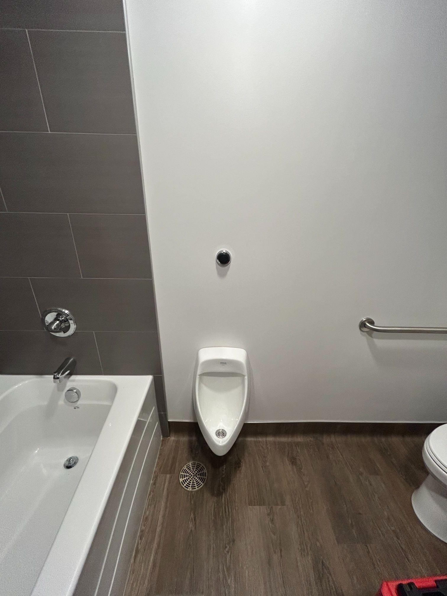 Bathroom with a bathtub, urinal, and toilet; dark wood floor, white walls, and gray tile.