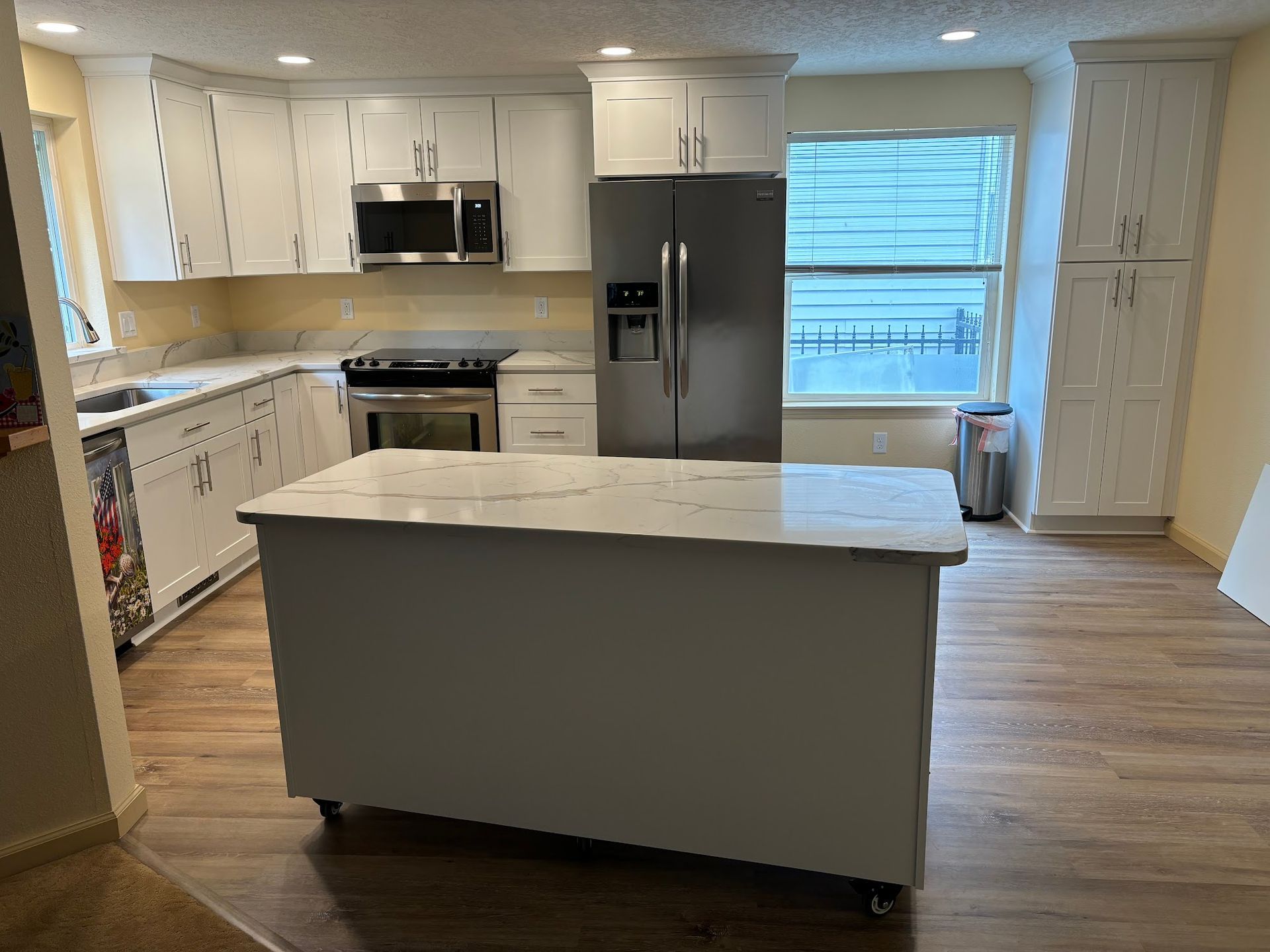 White kitchen with island, stainless steel appliances, and wood-look flooring.