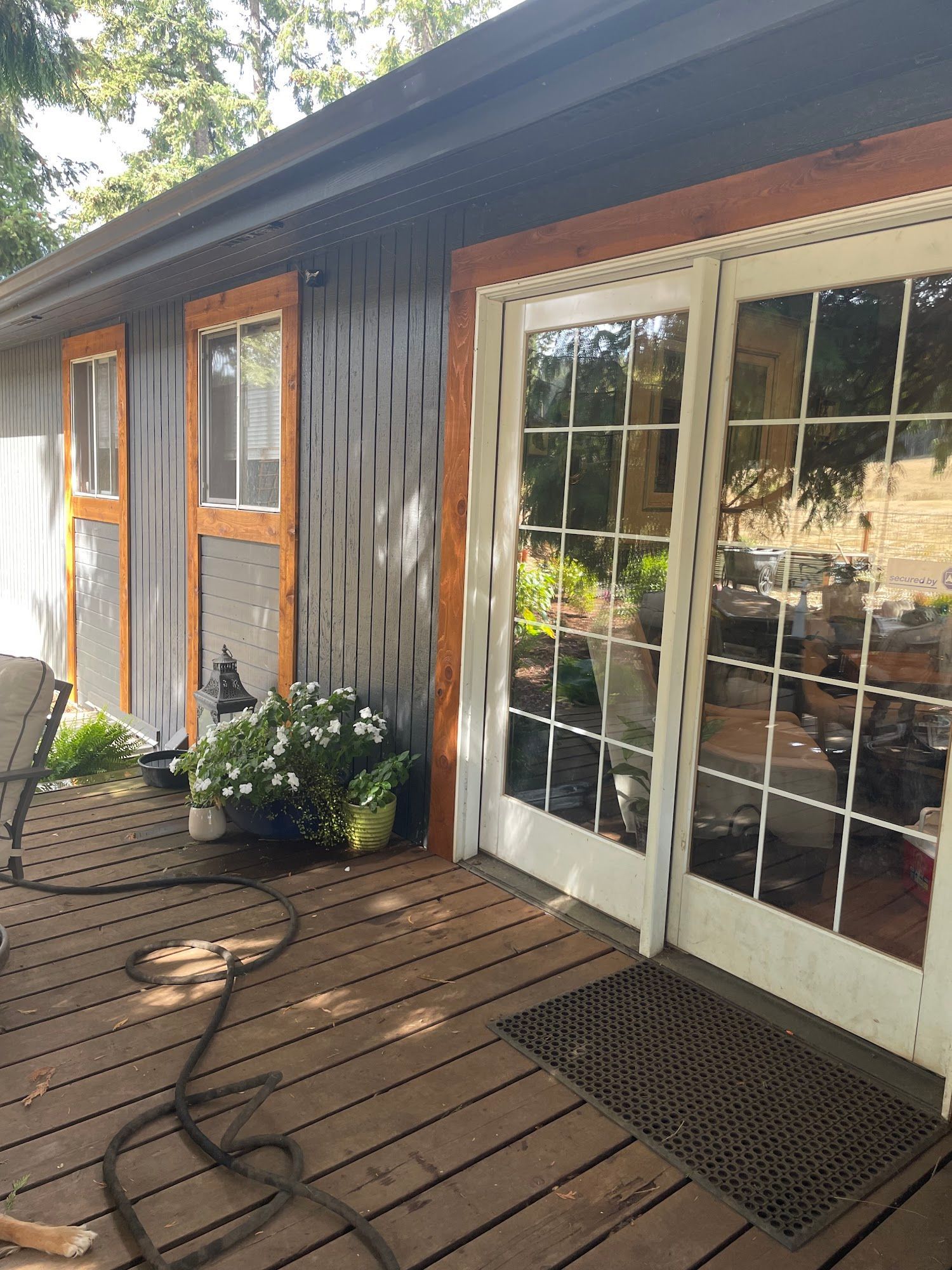 Wooden deck with gray siding, white French doors, and screen doors. A garden is in the background.