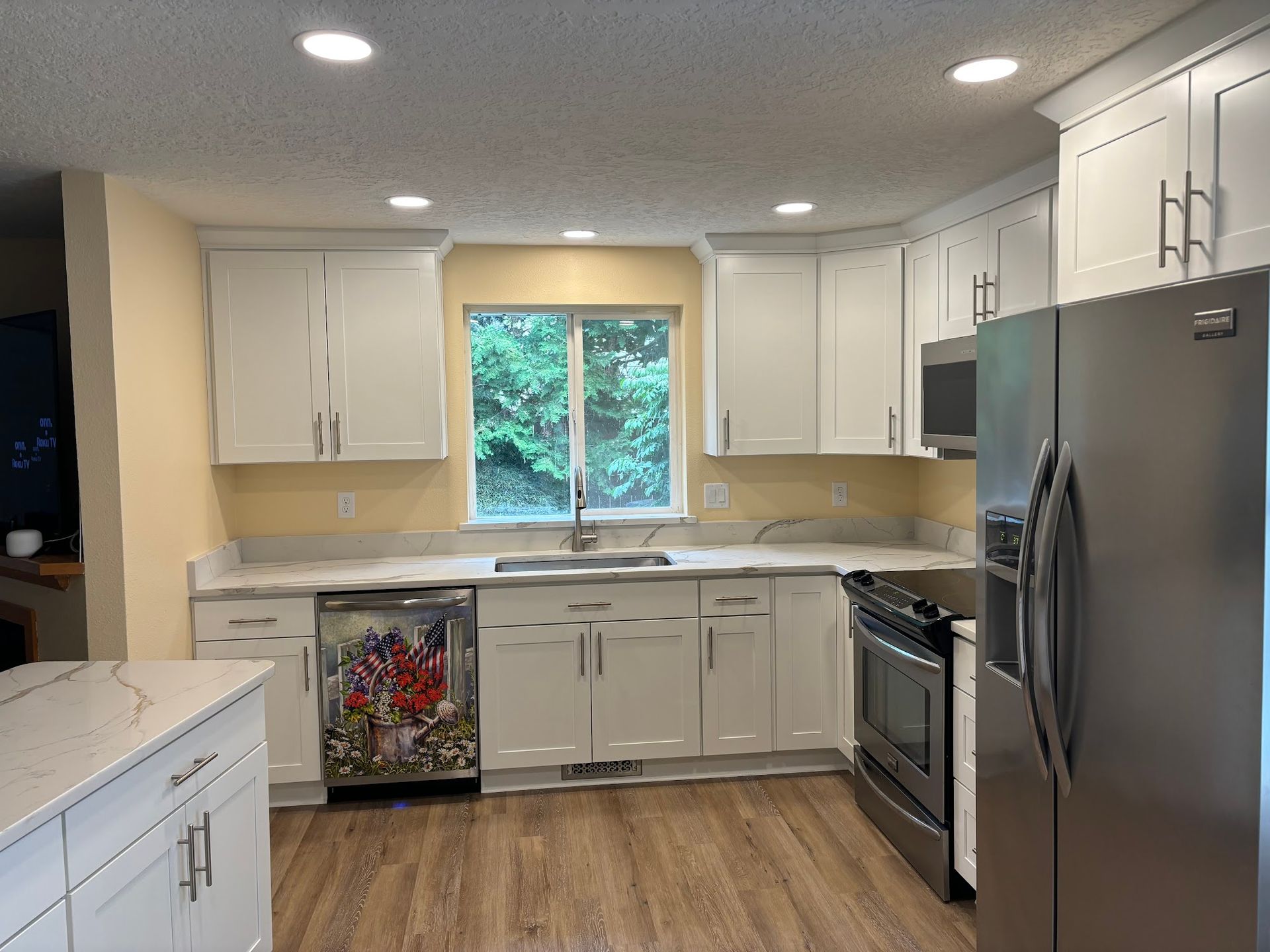 White kitchen with granite countertops, stainless steel appliances, and wood-look flooring.