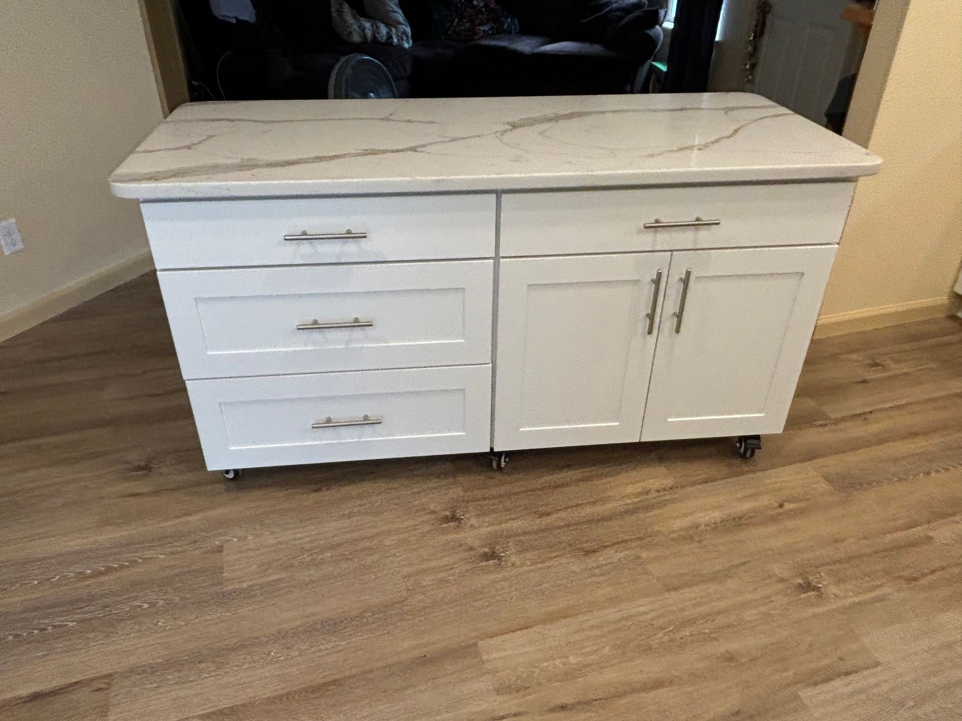 White kitchen island with marble countertop on wooden floor.