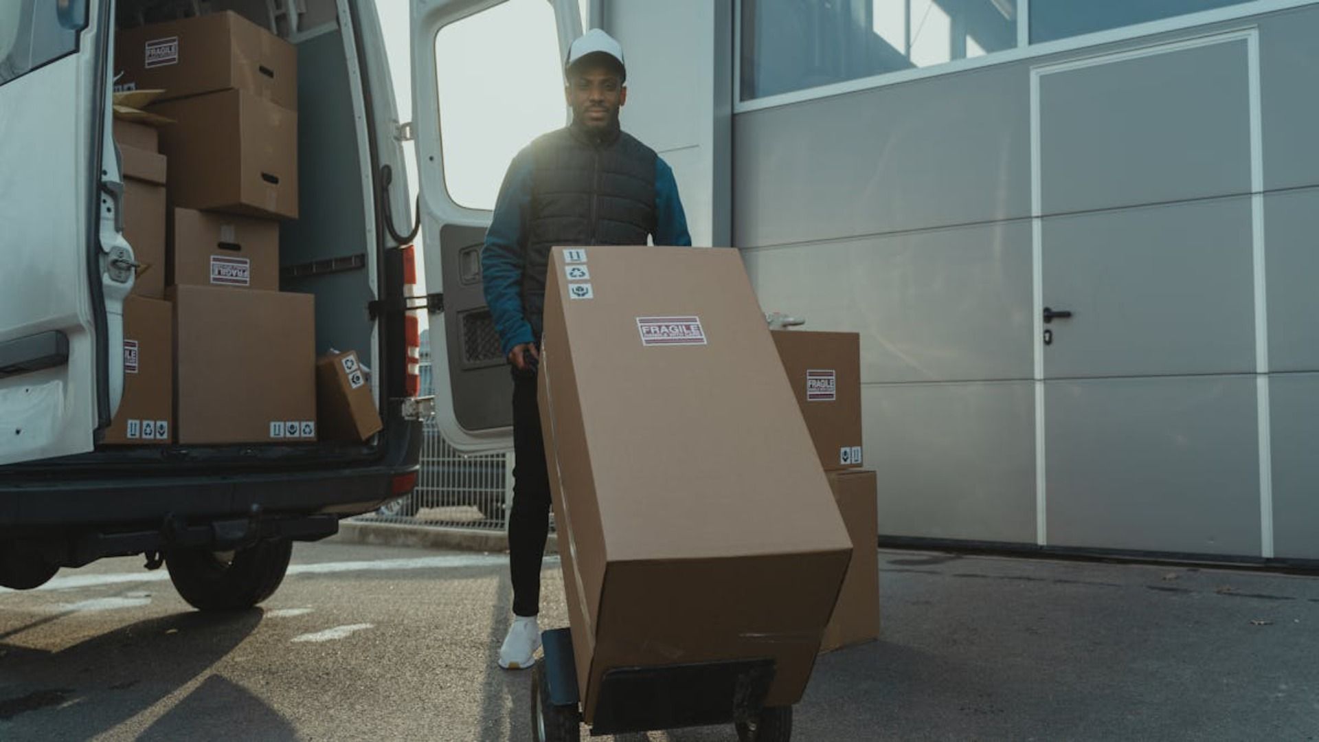 Un hombre empuja un carrito con cajas delante de una camioneta.