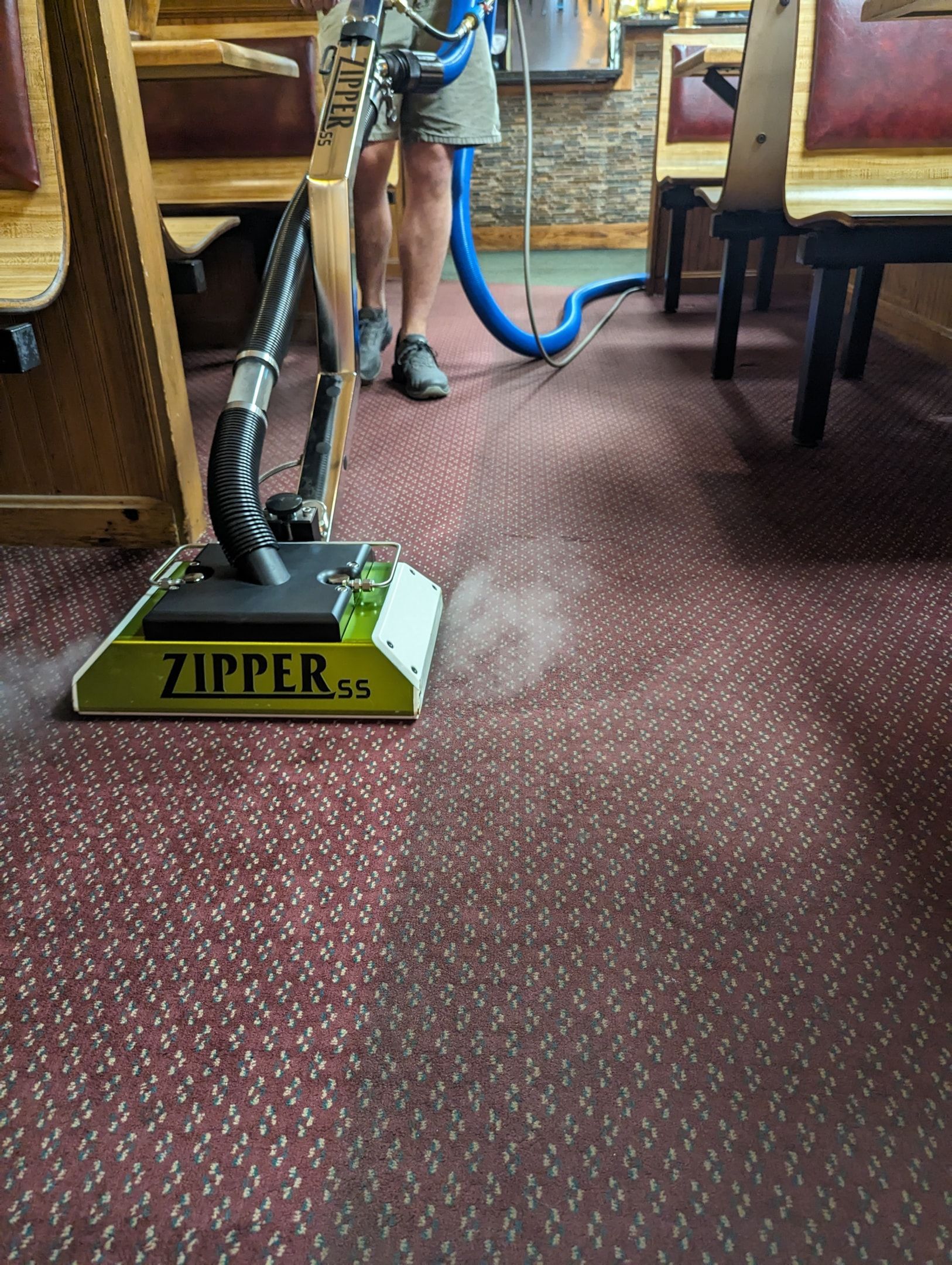 A man is using a vacuum cleaner to clean a carpet in a restaurant.