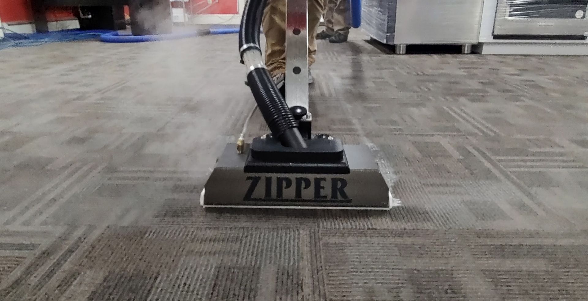 A person is using a zipper vacuum cleaner to clean a carpeted floor.