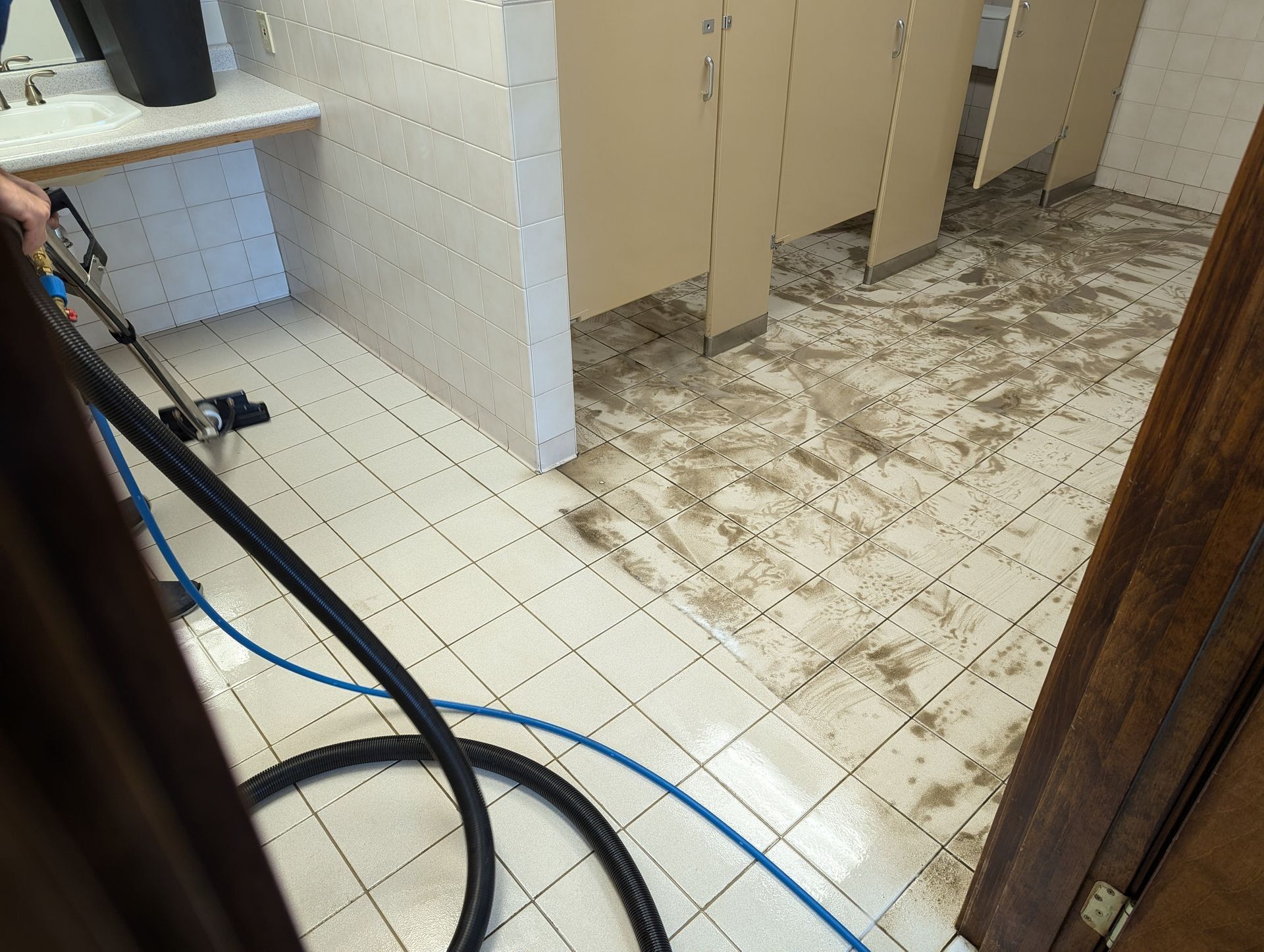 A person is cleaning a bathroom floor with a vacuum cleaner.