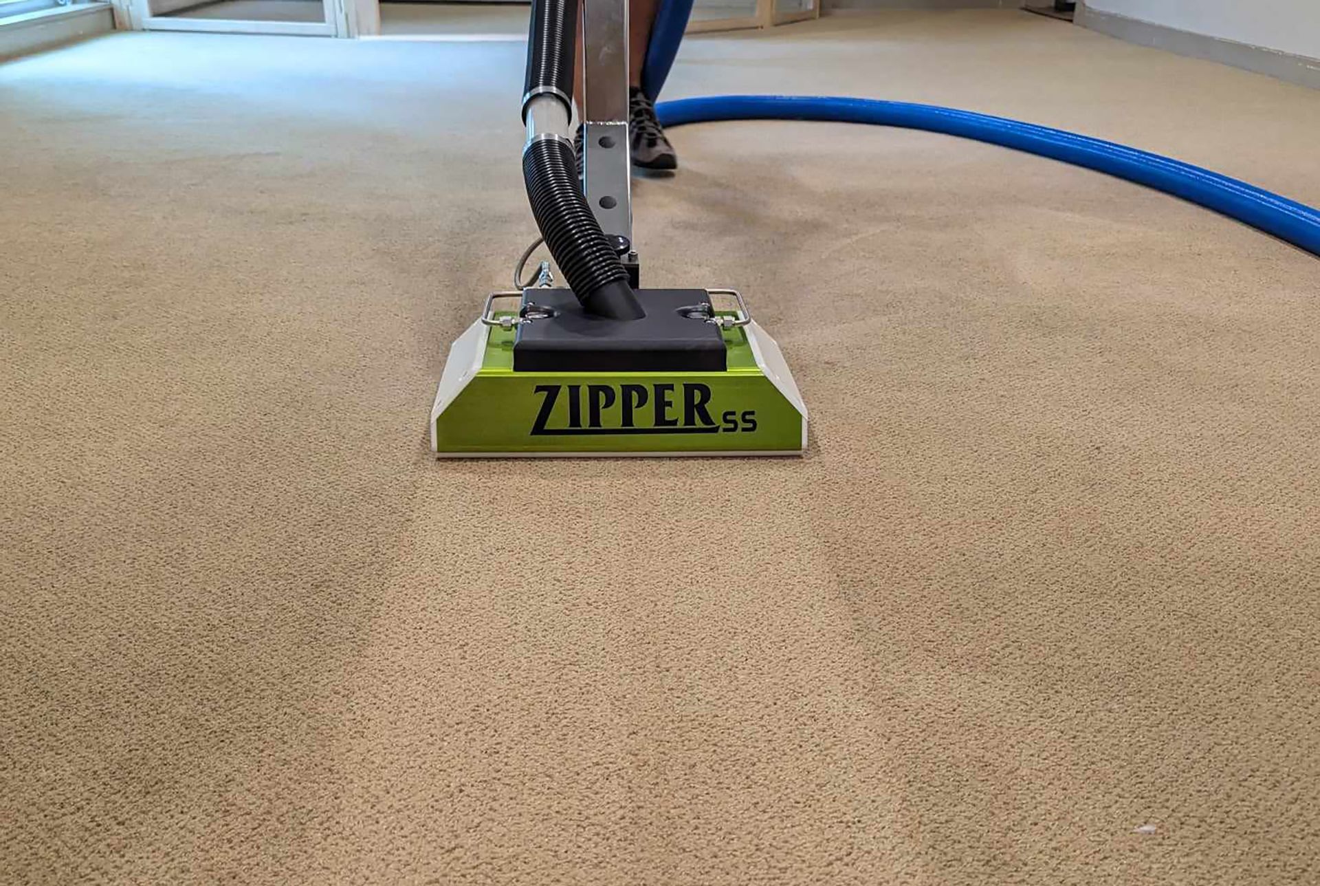 A person is cleaning a carpet with a zipper vacuum cleaner.