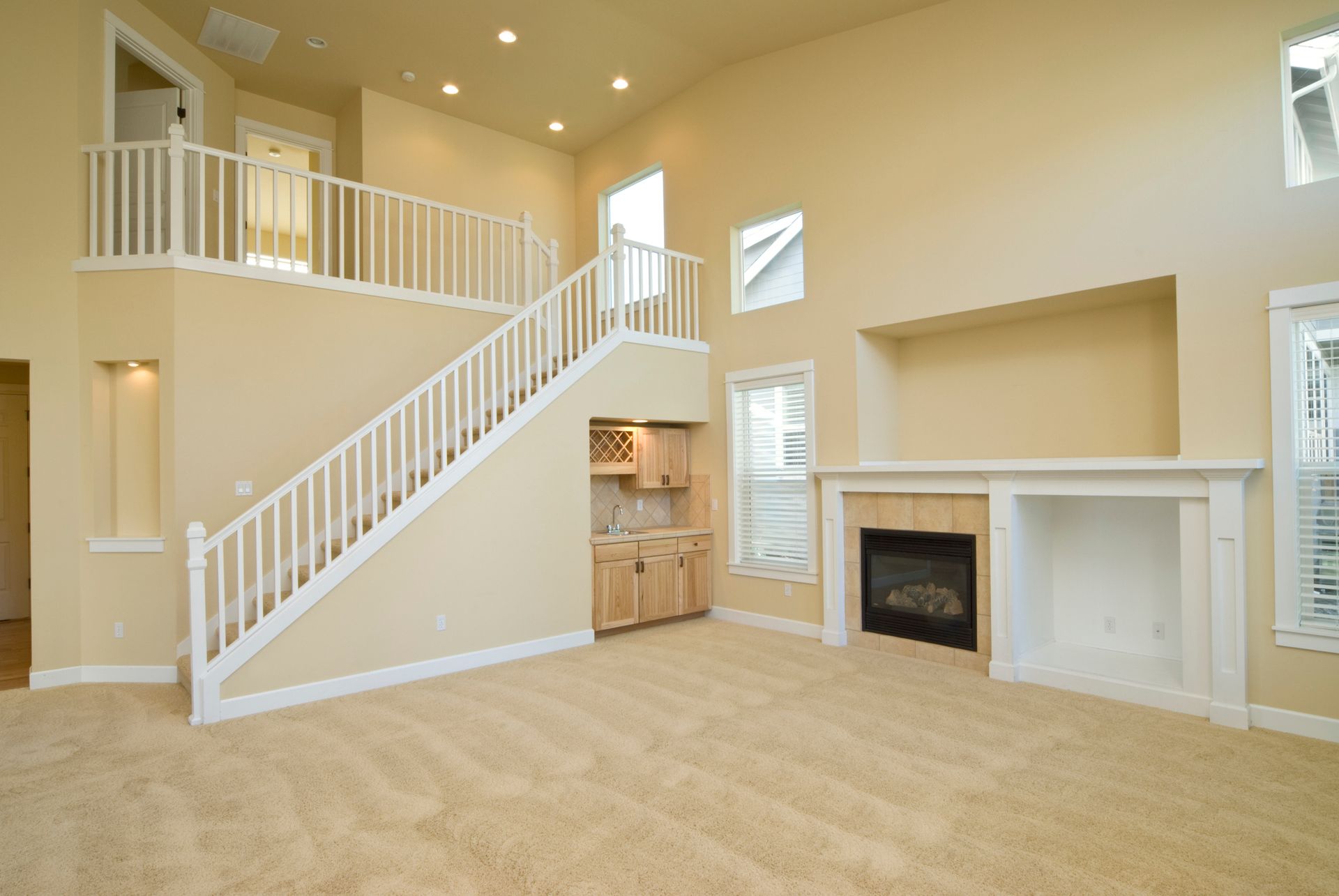 An empty living room with stairs leading up to the second floor and a fireplace.