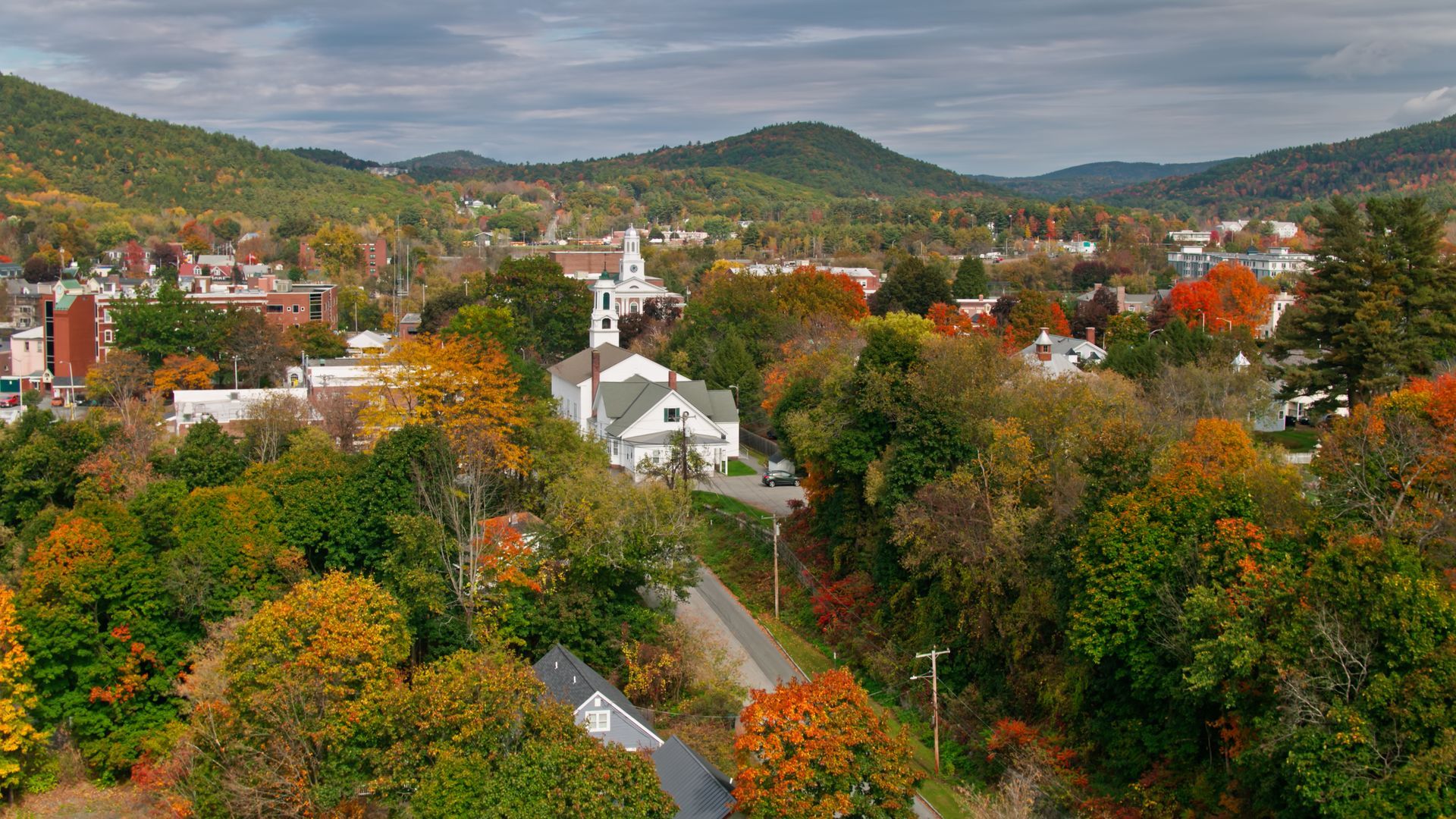 A New England town in autumn, featuring colorful trees, a white church, and rolling hills.