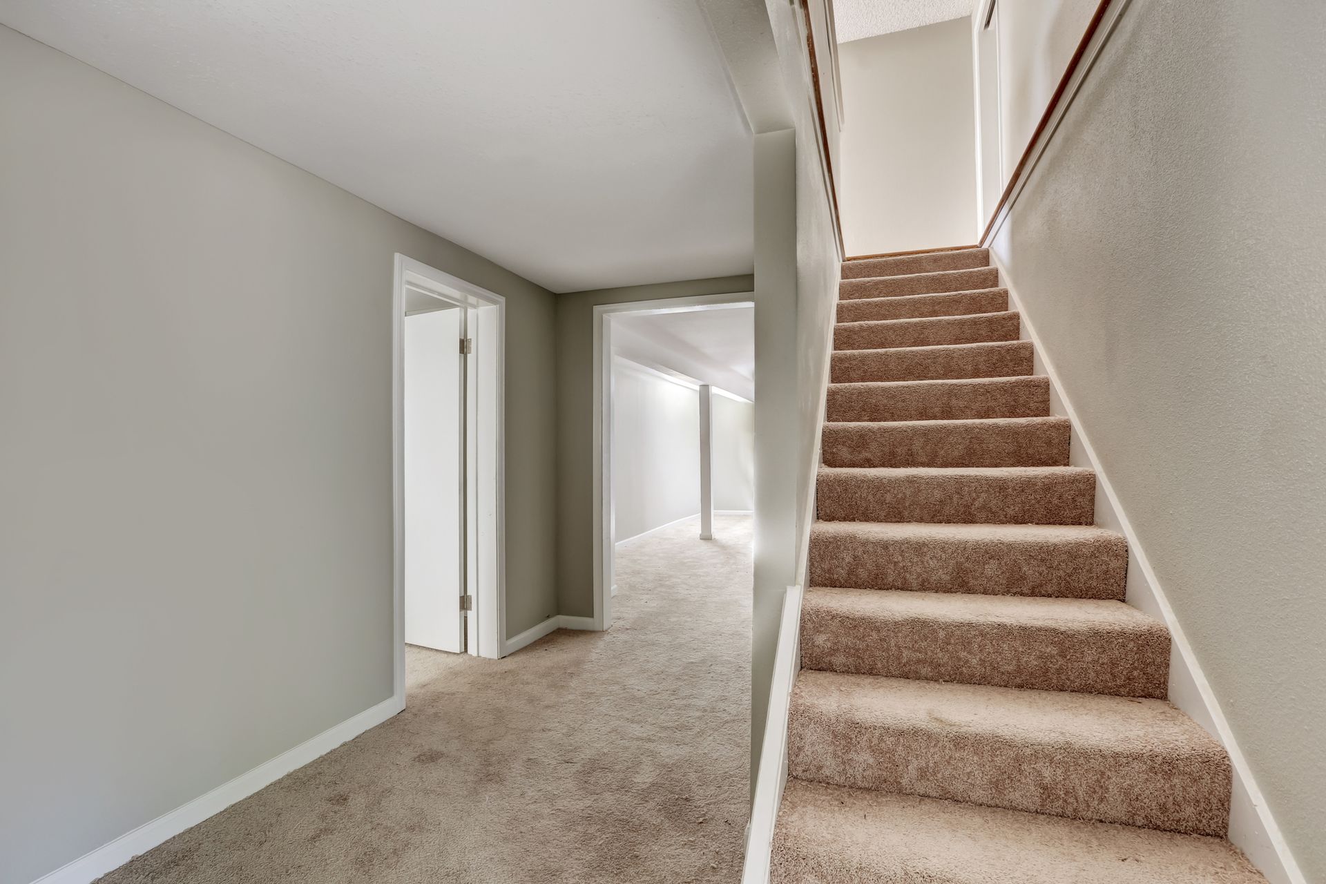 Hallway with carpeted stairs and doors; light gray walls and beige carpet.