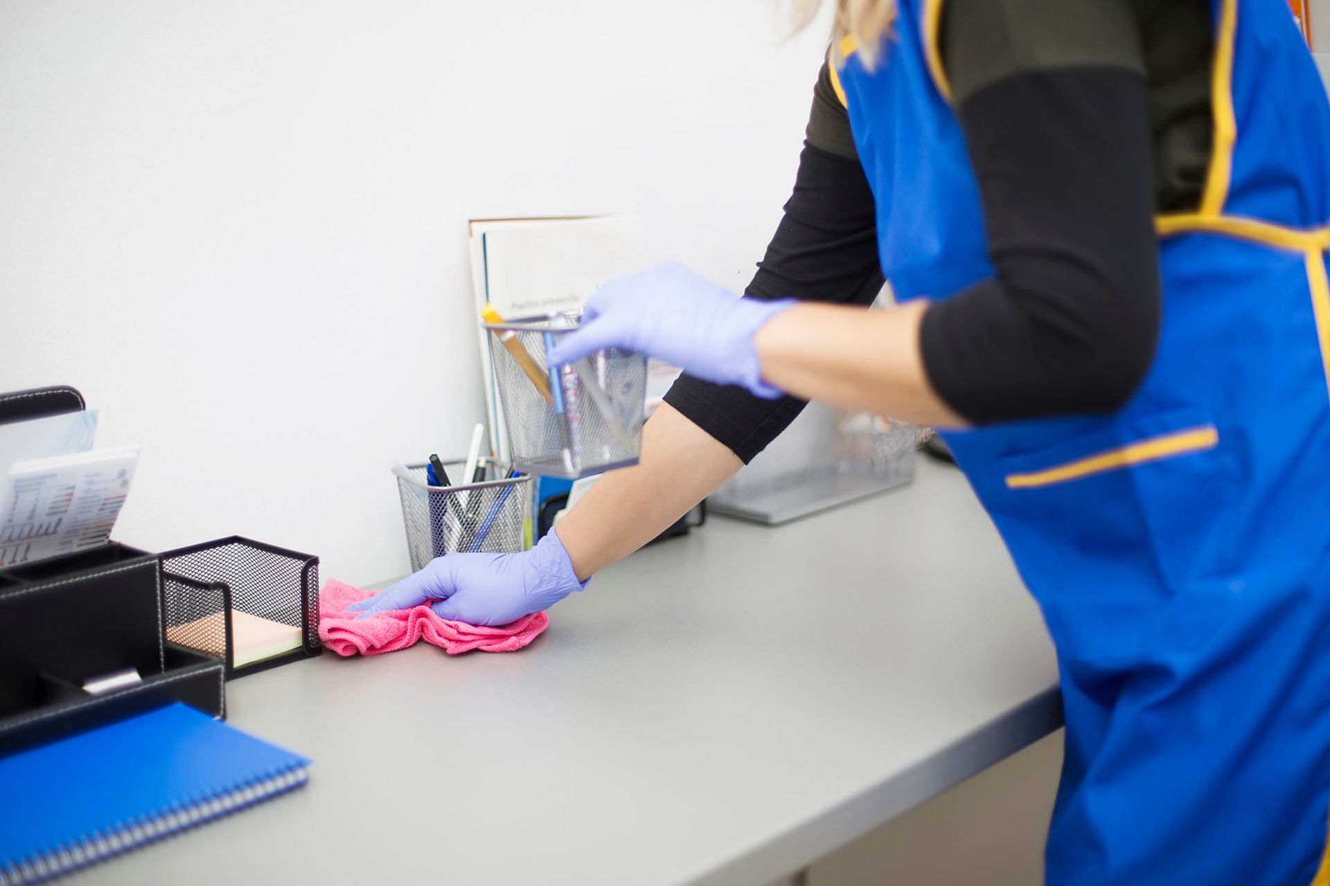 A woman in a blue apron and gloves is cleaning a desk.