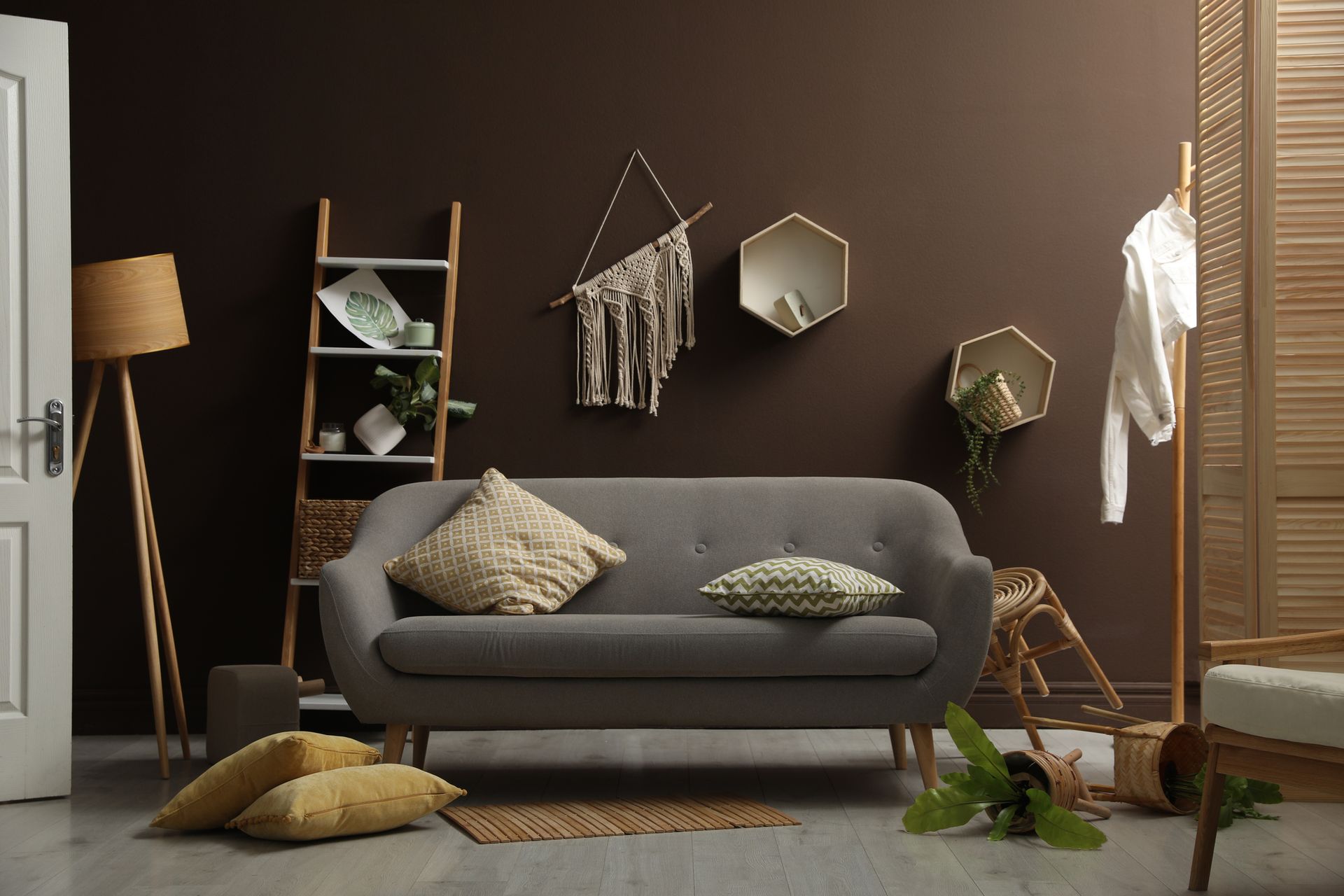 Cozy living room with gray sofa, hanging wall decor, shelves, plants, and warm brown walls