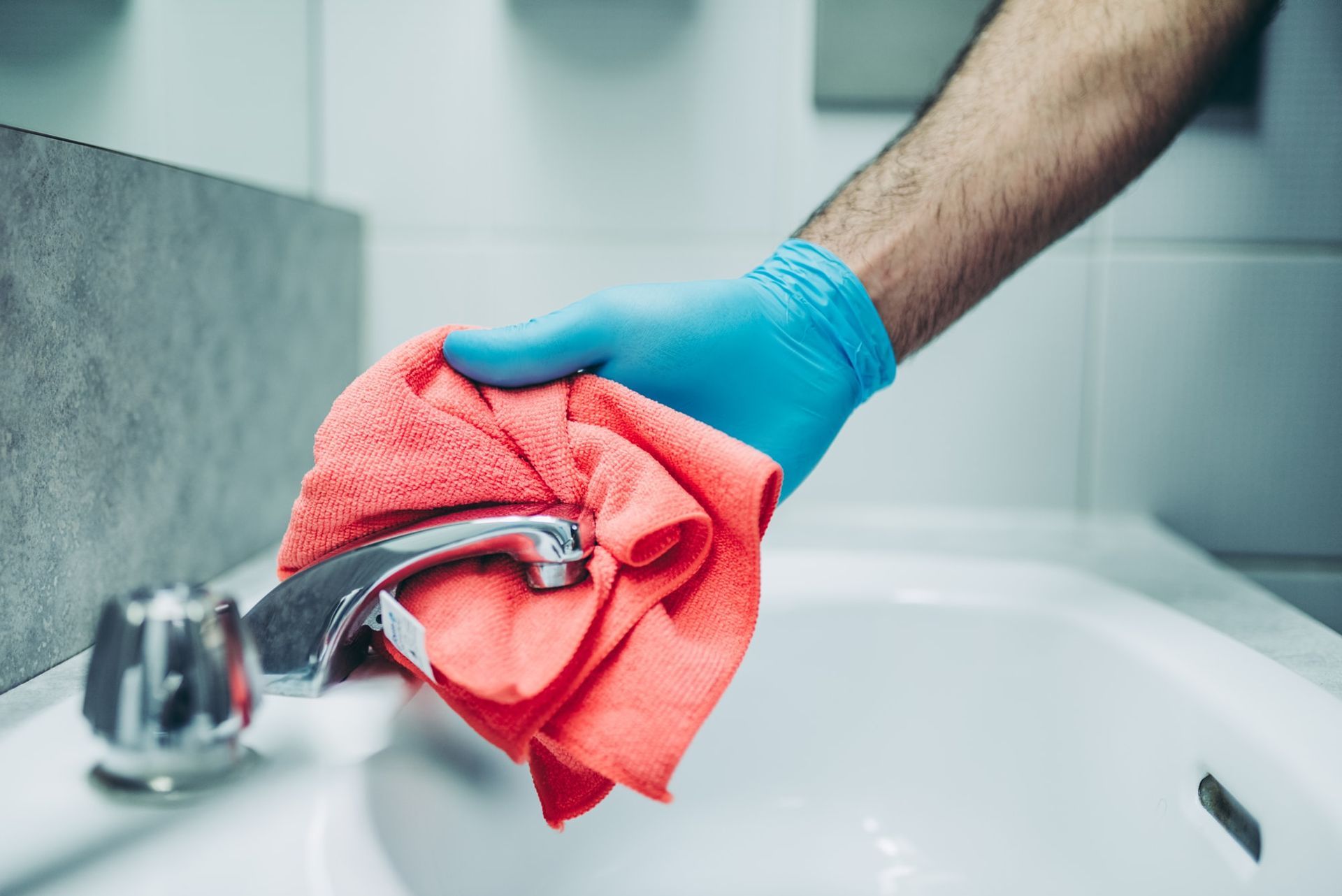 A person wearing blue gloves is cleaning a sink with a towel.