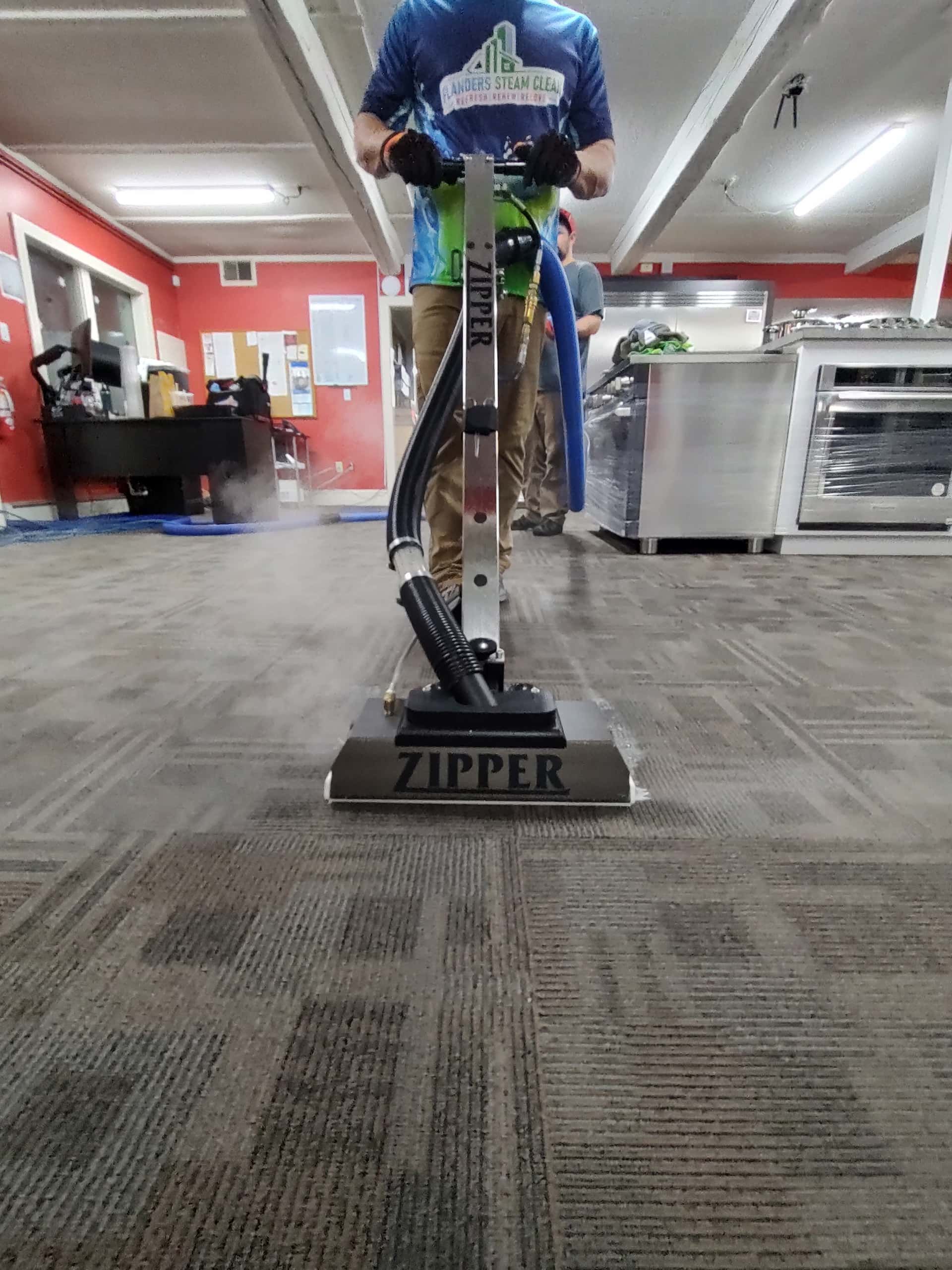 A man is using a zipper vacuum cleaner to clean a carpeted floor.