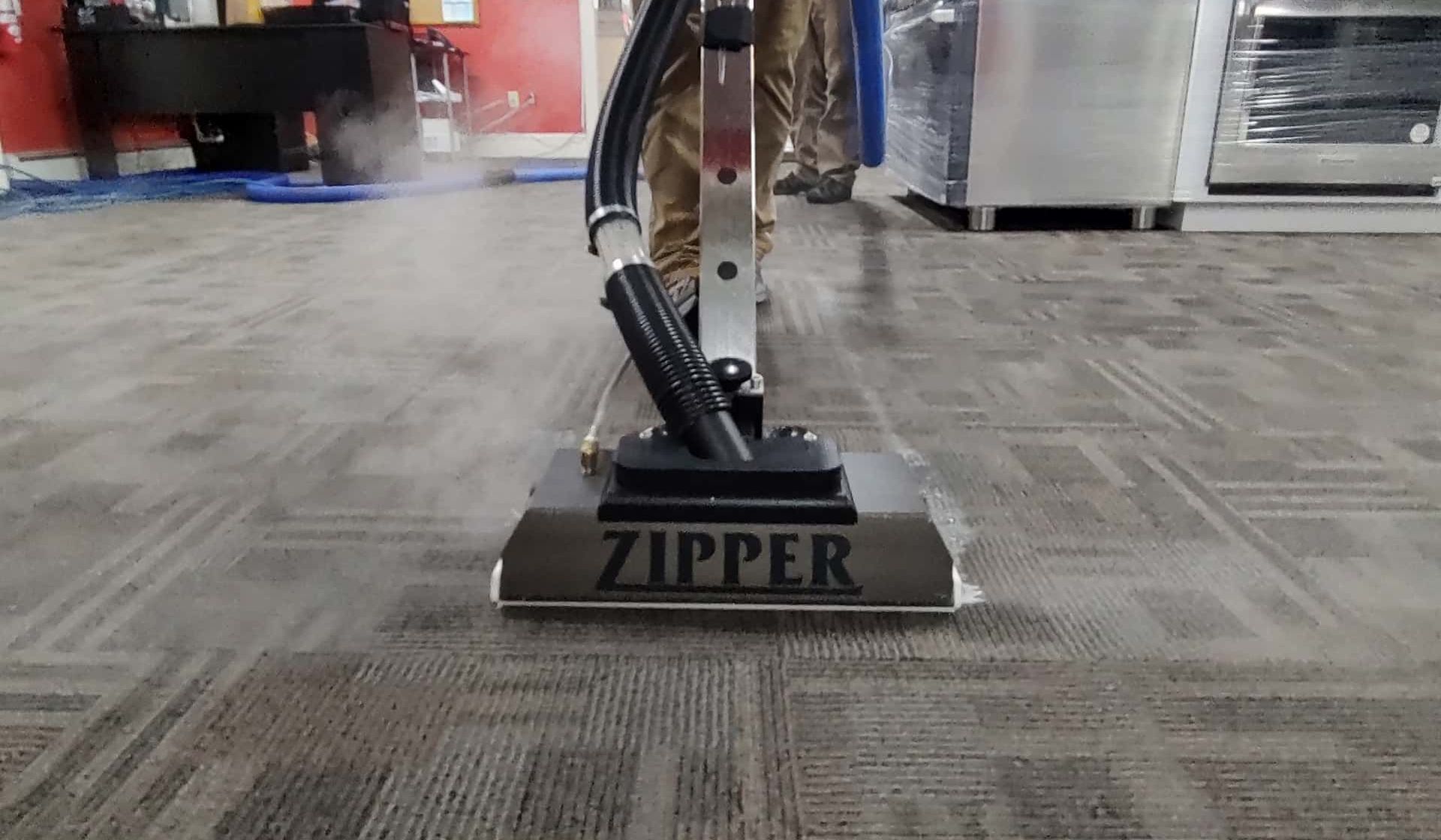 A person is using a zipper vacuum cleaner to clean a carpet.