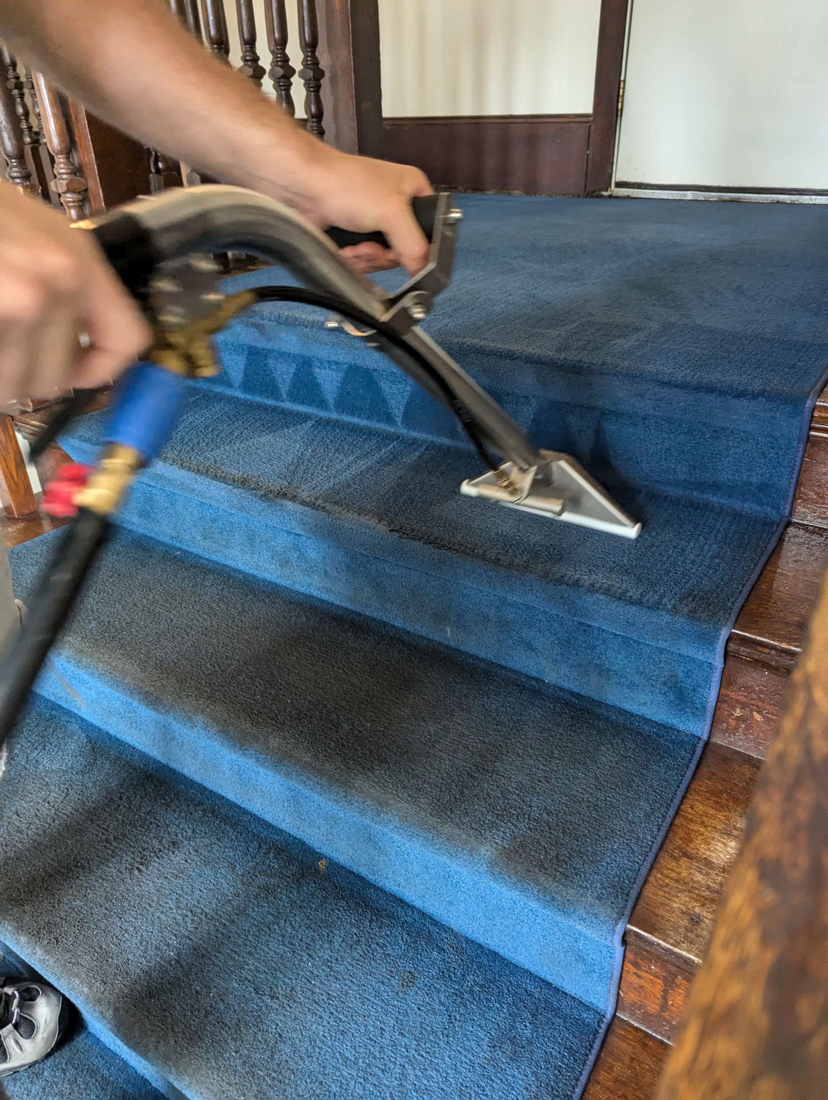 A person is cleaning a blue carpeted staircase with a vacuum cleaner.