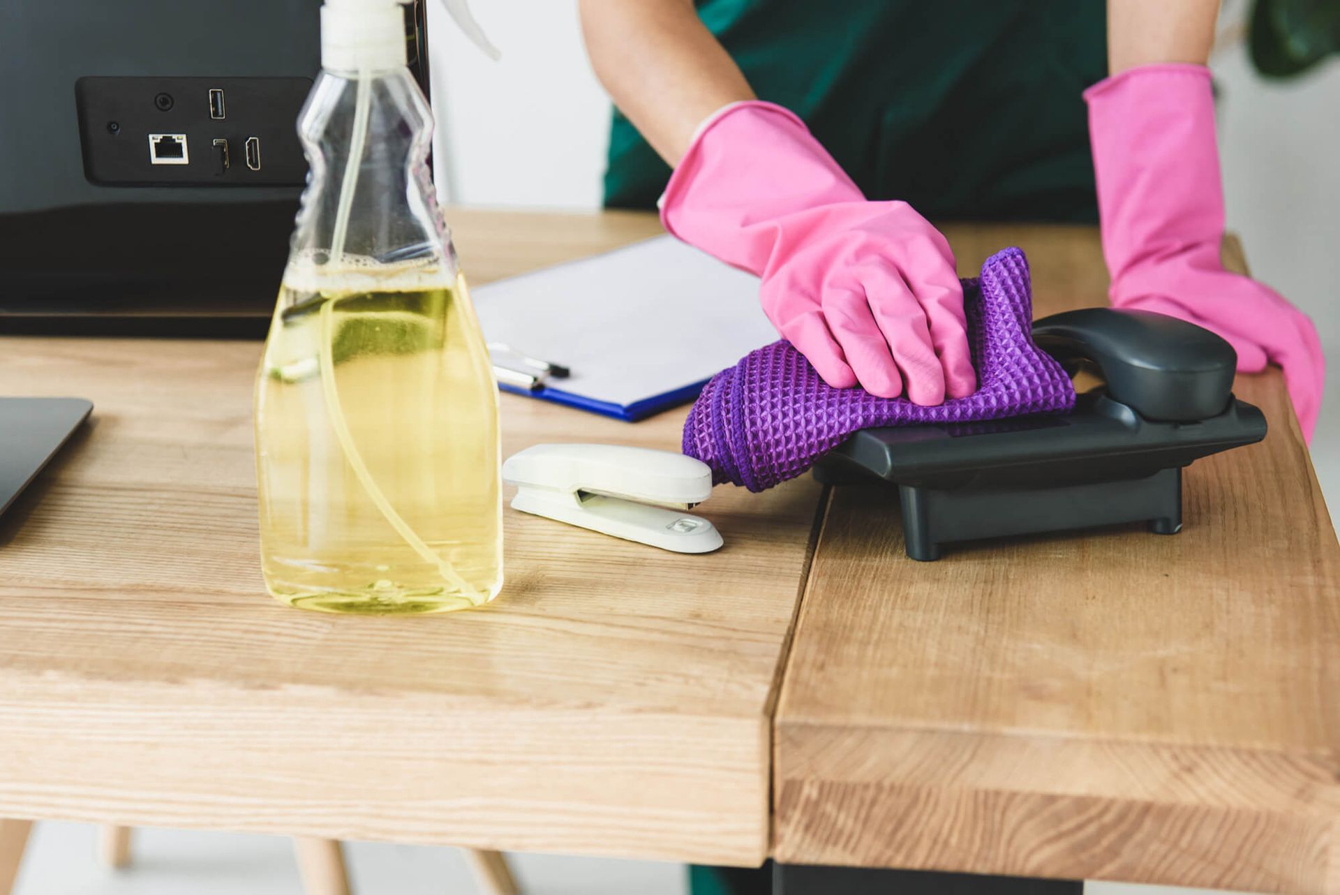 A person wearing pink gloves is cleaning a telephone on a desk.