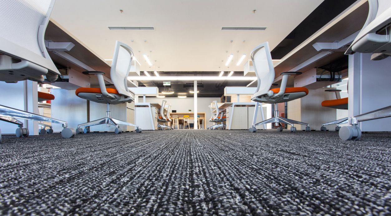 A close up of a carpeted floor in an office with desks and chairs.