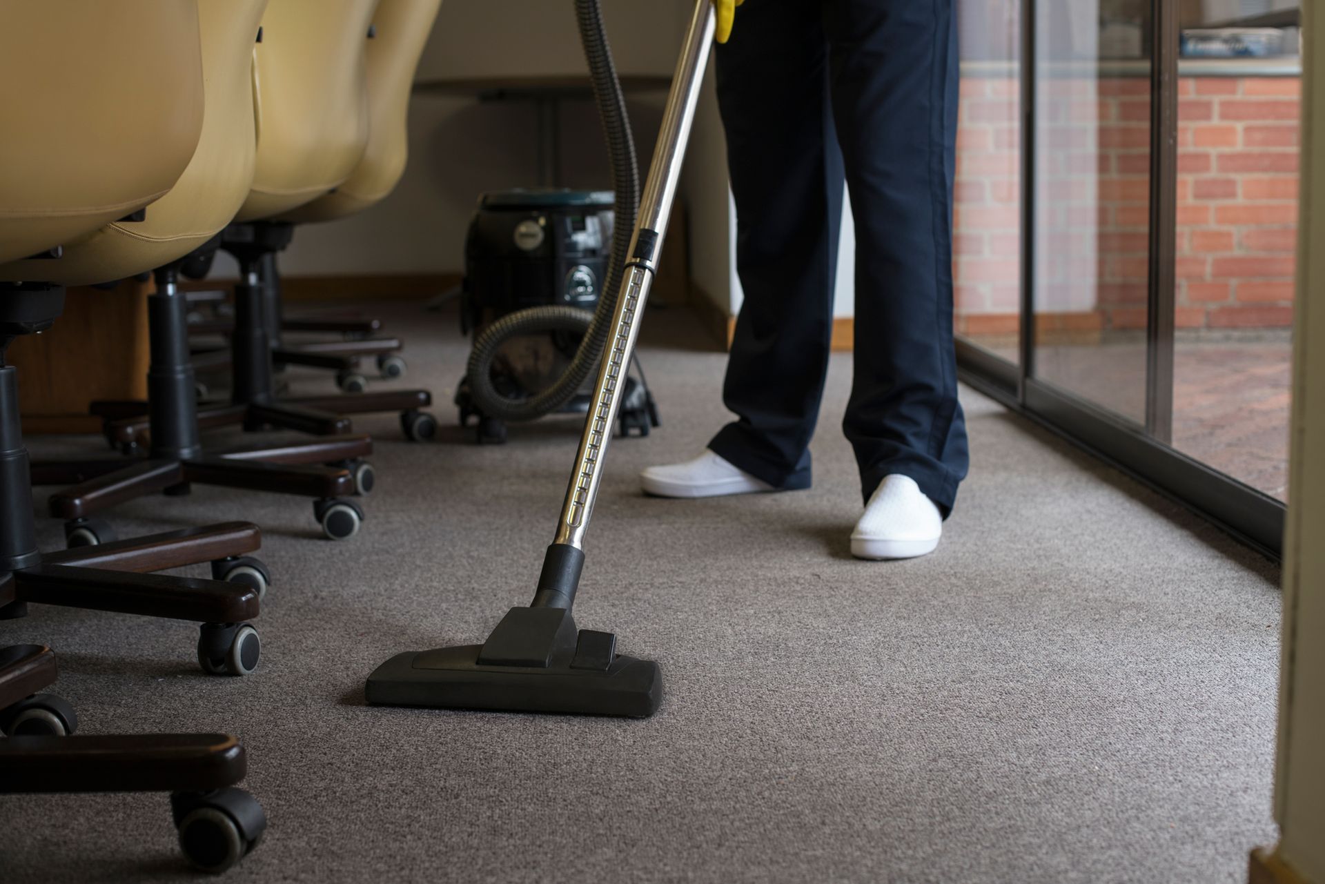 A person is using a vacuum cleaner to clean a carpet in an office.