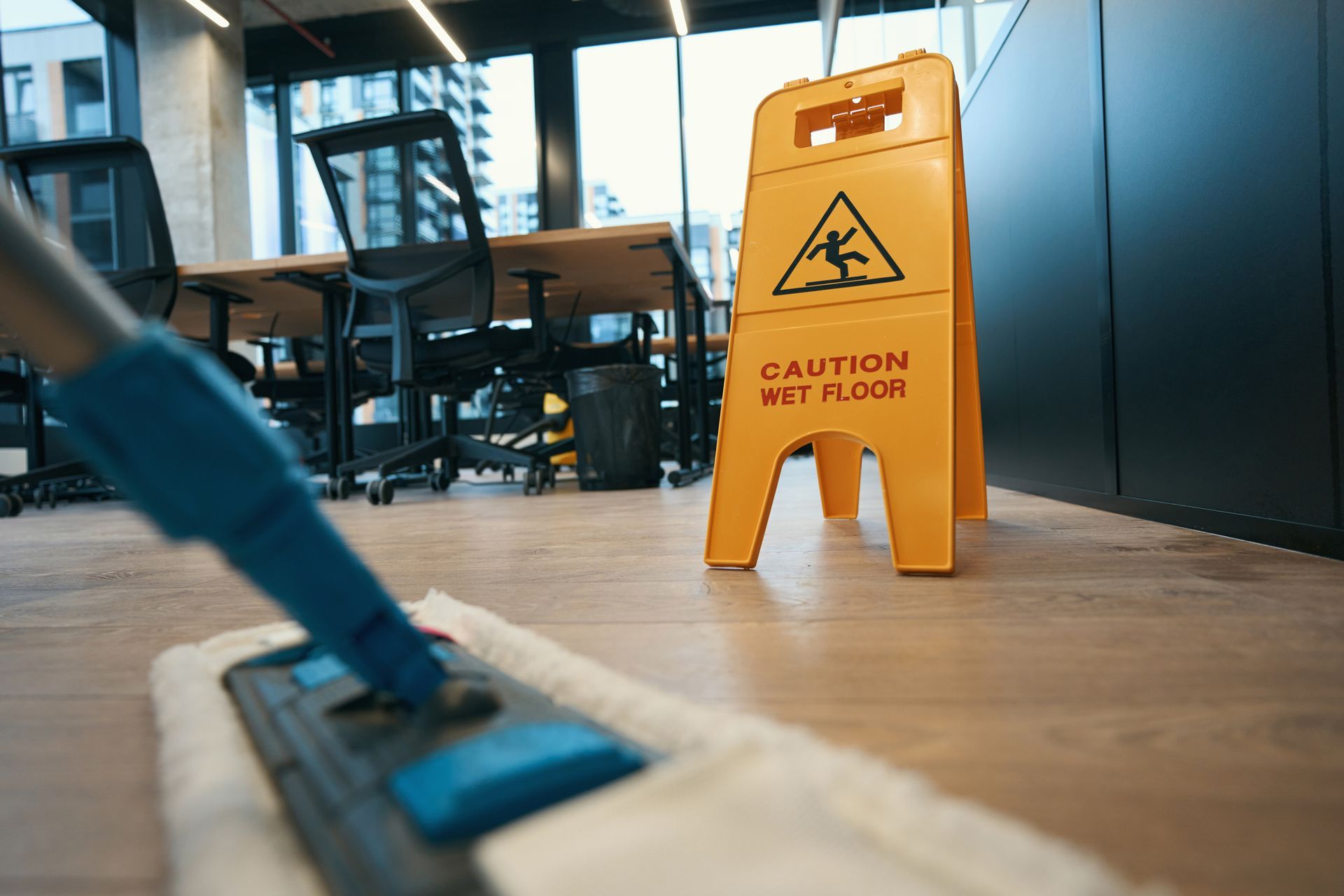 A mop is being used to clean an office floor next to a caution wet floor sign.