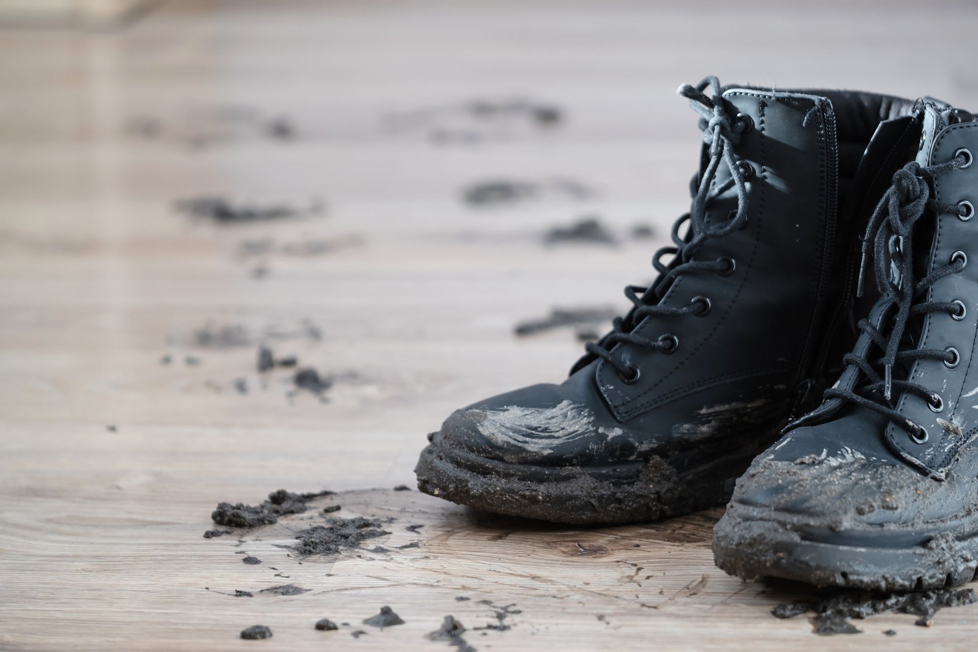 Dirty black boots on a wood floor, with muddy footprints trailing away.