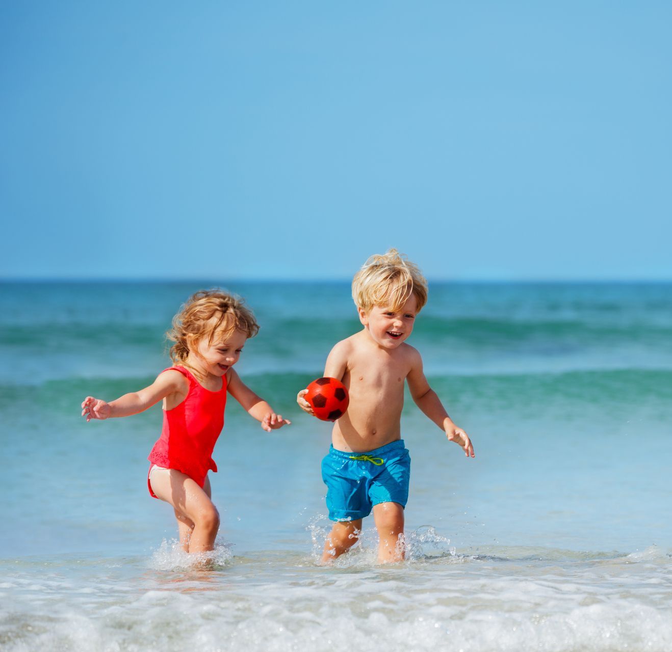 Two children running through water on a beach.