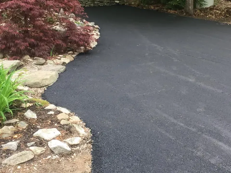 A black asphalt driveway surrounded by rocks and plants.