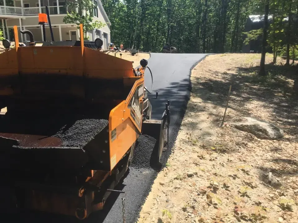 A machine is laying asphalt on a driveway in front of a house.