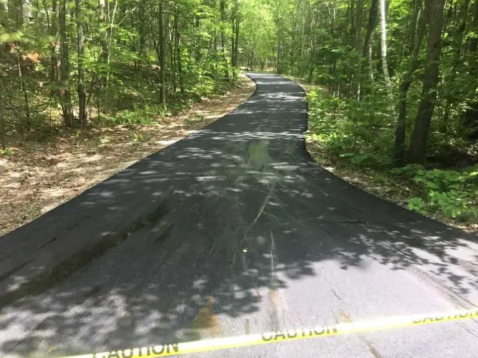 A road with a caution tape on it is surrounded by trees.