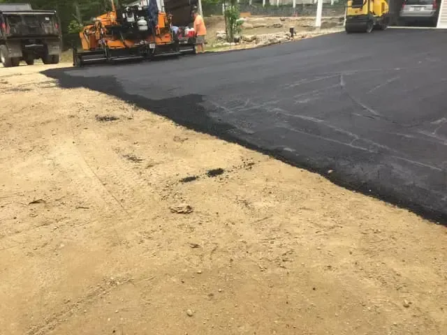 A machine is laying asphalt on a dirt road.