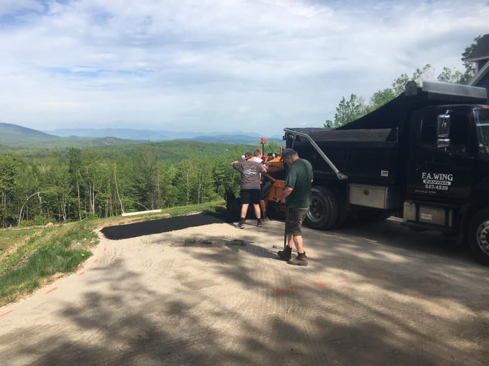A group of people are standing next to a dump truck on a dirt road.