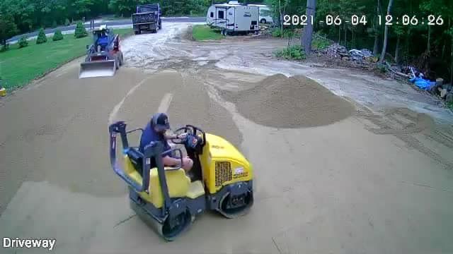 A man is driving a yellow roller on a dirt road.