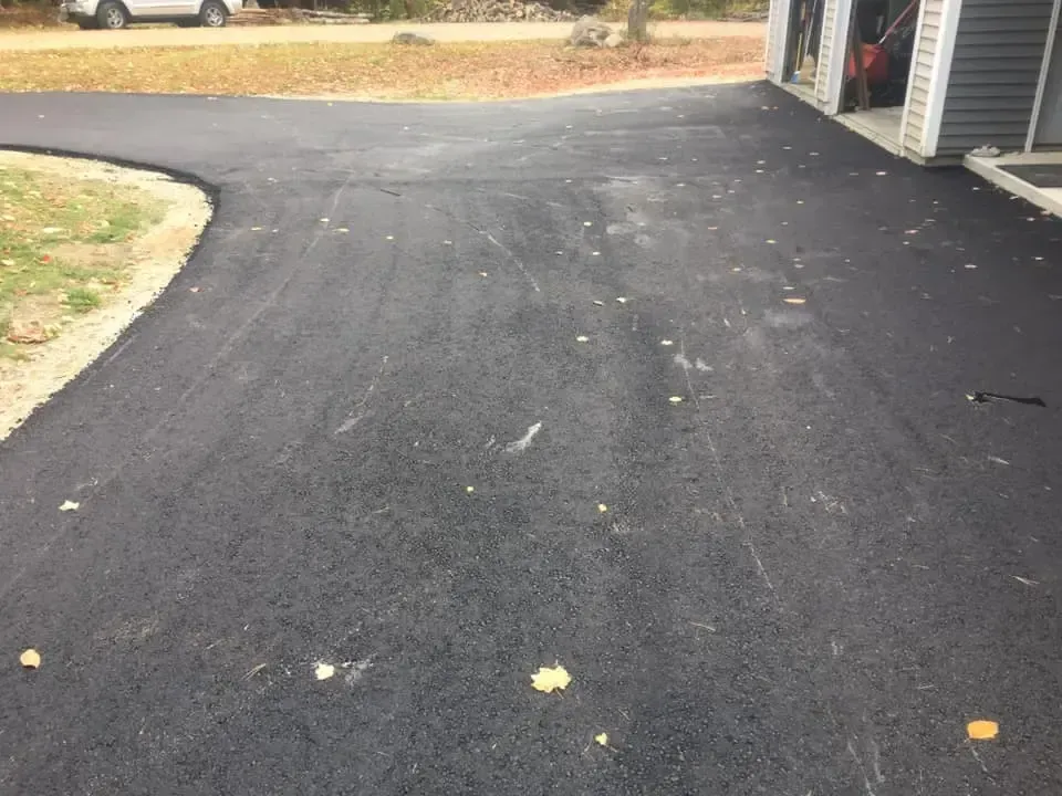 A black asphalt driveway with a white car parked on the side of it.
