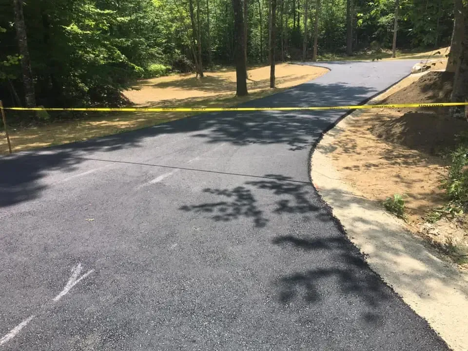 A newly paved driveway is surrounded by trees and tape.