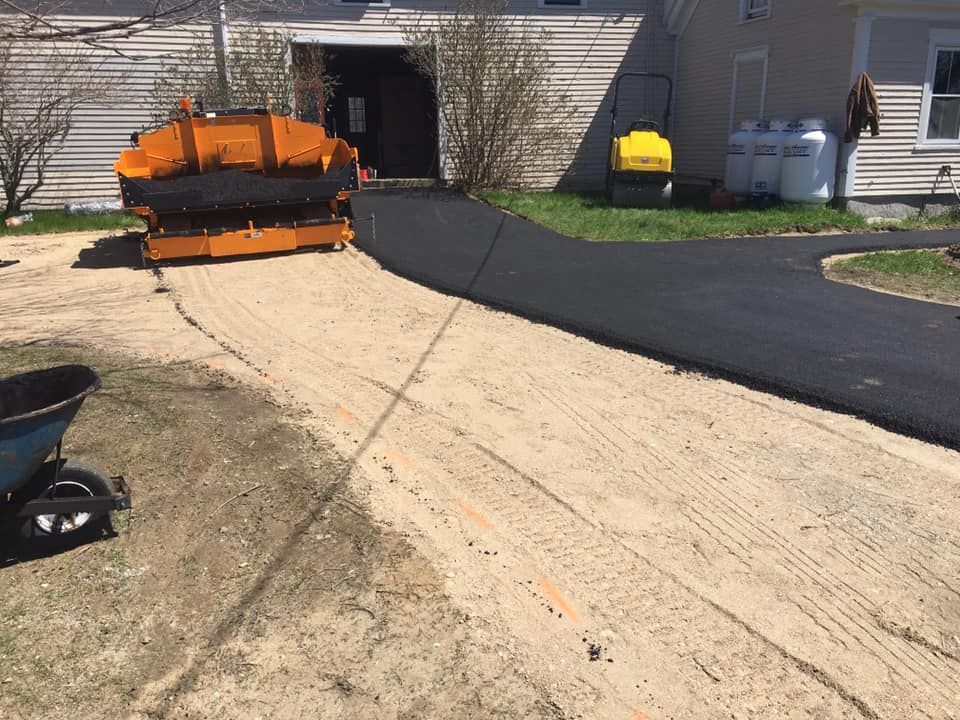 A machine is laying asphalt on a driveway in front of a house.