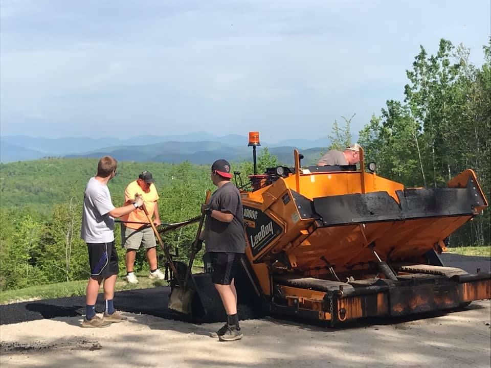 A group of men are working on a road with a tractor in the background.