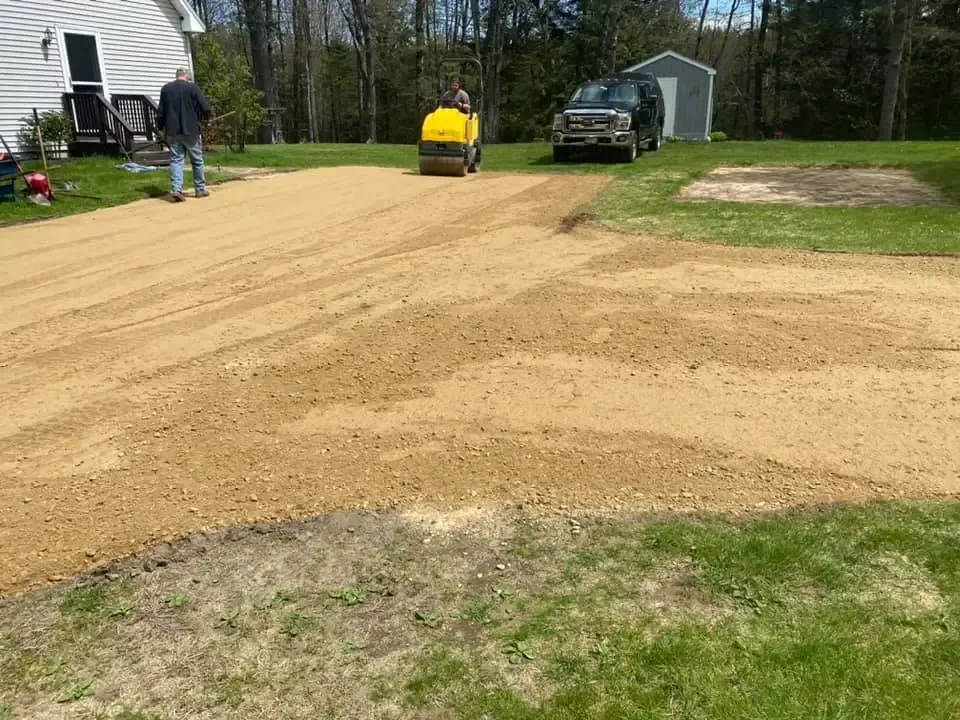 A man is standing next to a yellow roller on a dirt road.