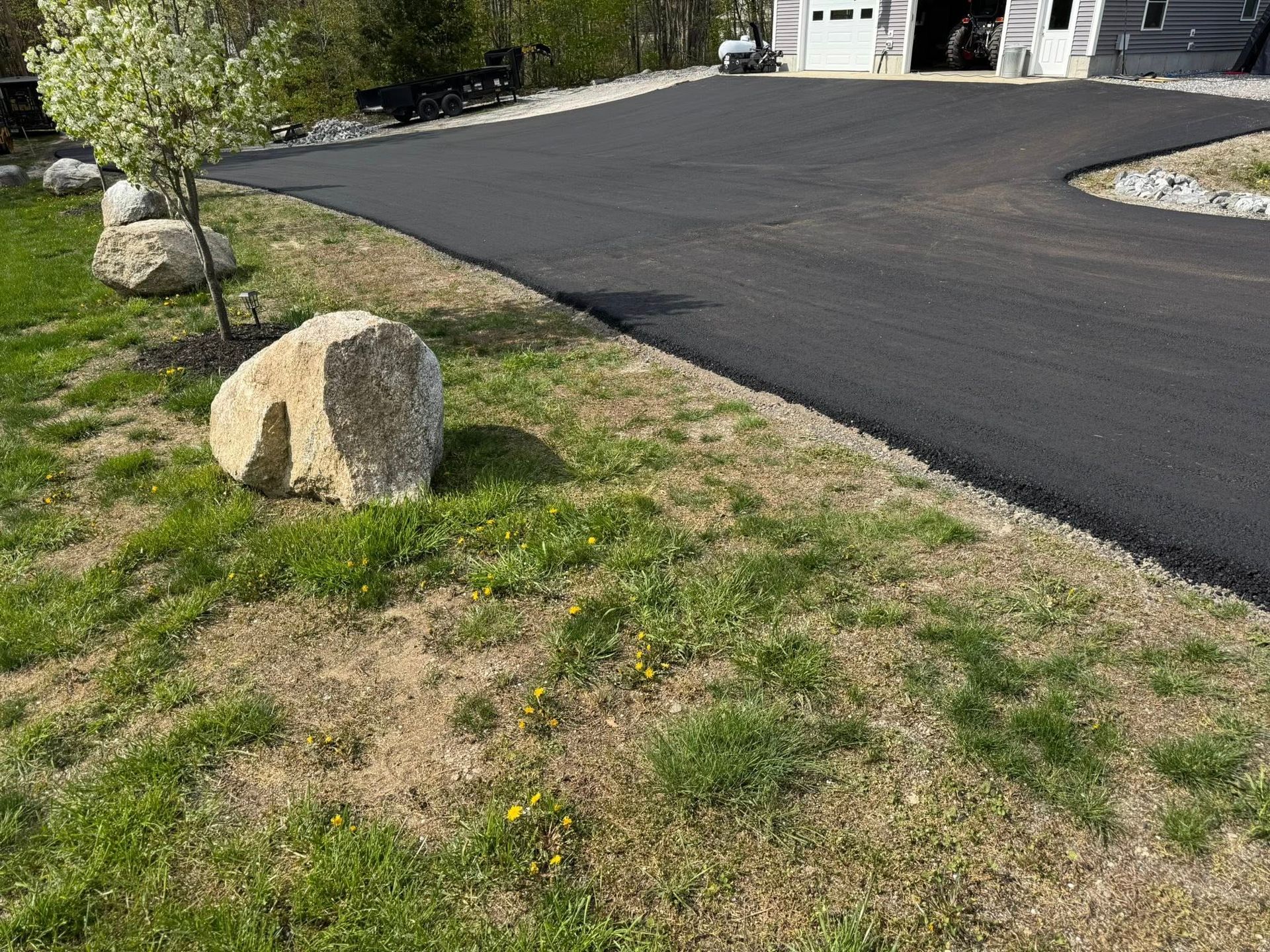 A large rock is sitting in the grass next to a driveway.