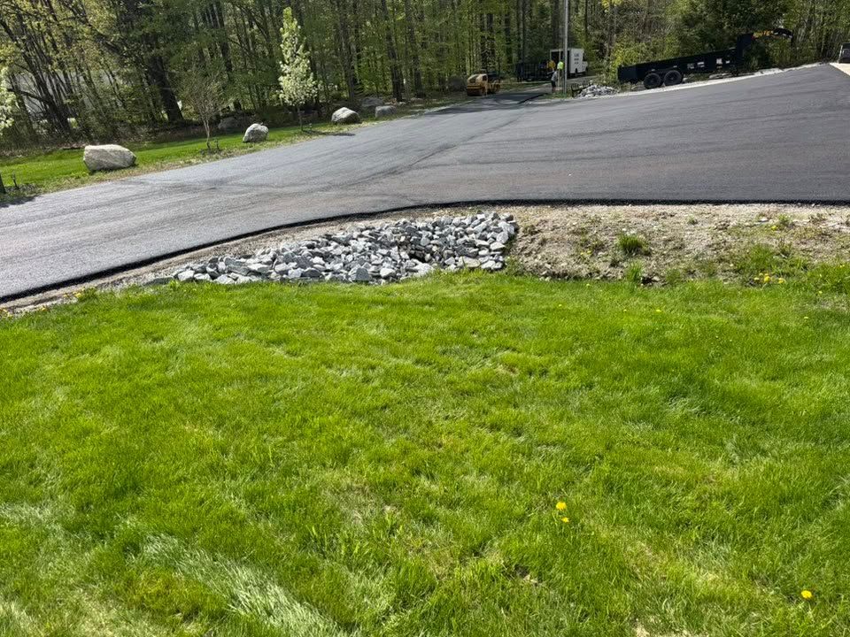A lush green lawn next to a road with trees in the background.
