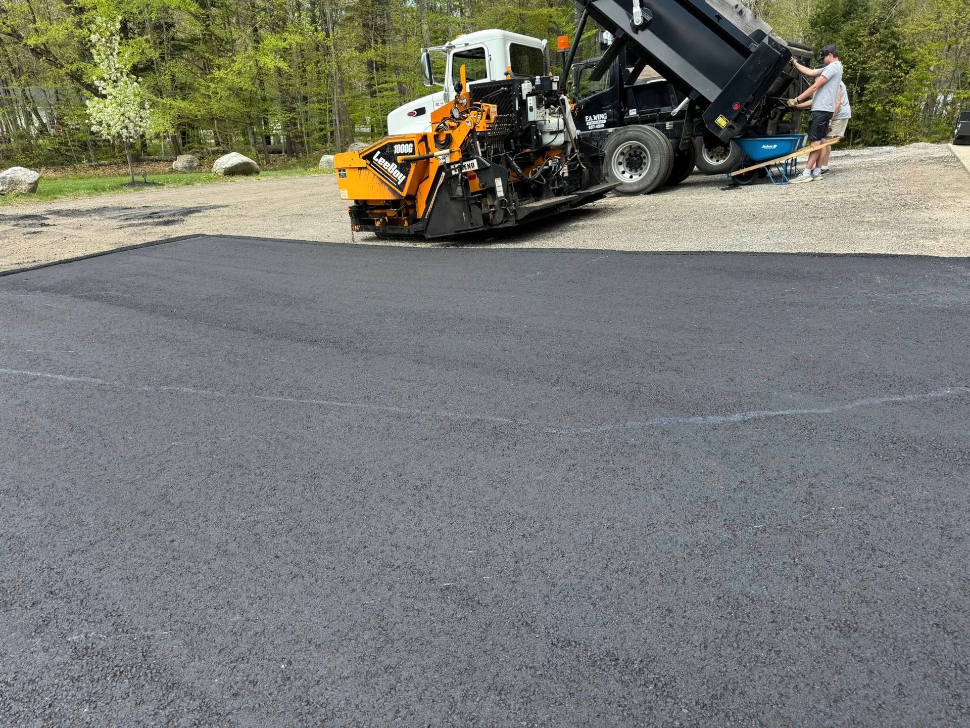 A dump truck is being loaded with asphalt in a parking lot.
